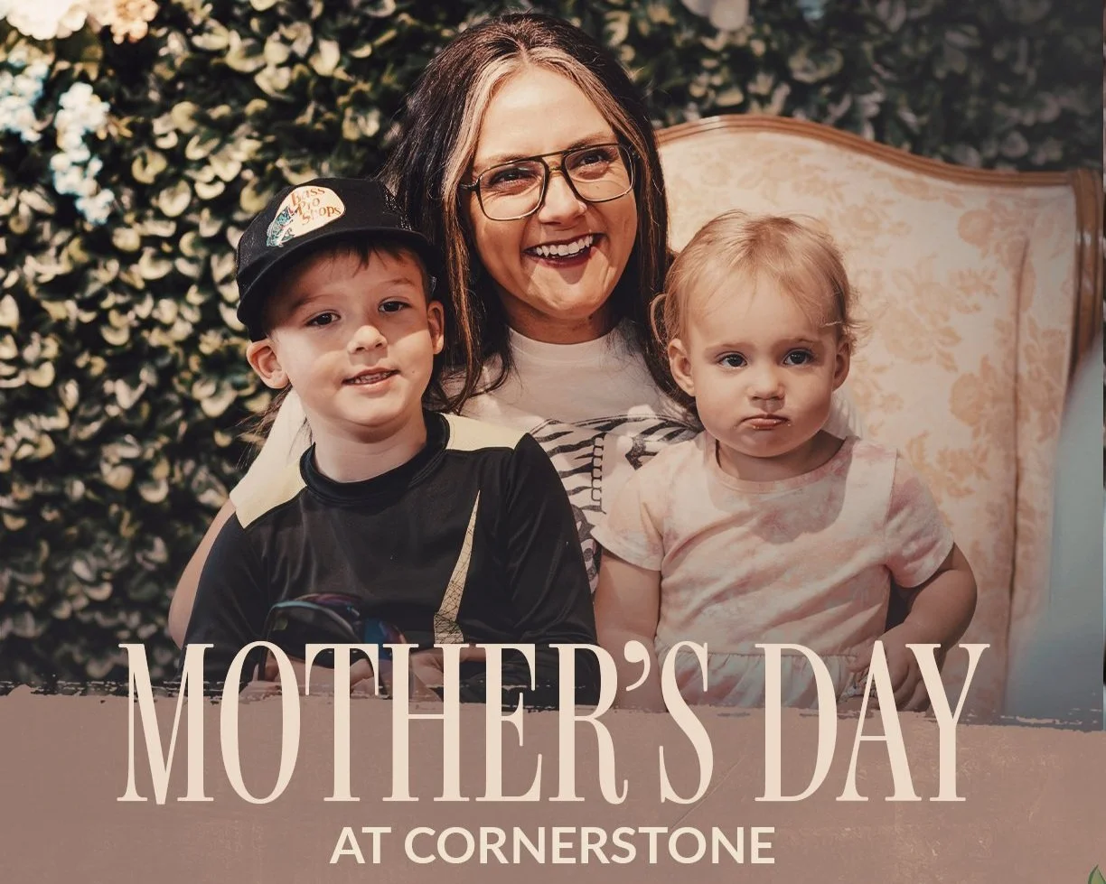 A woman with glasses smiling and sitting with two young children, a boy and a girl, in front of a floral backdrop, celebrating Mother's Day at Cornerstone.
