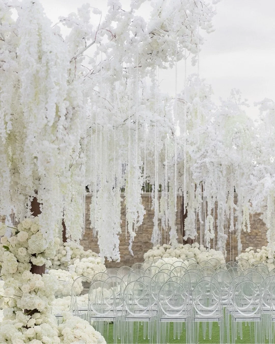 A white-on-white ceremony space suspended in a dream.

These images capture the essence of whimsical romance with a breathtaking canopy of oversized floral trees, their branches dripping in cascades of white wisteria and delicate crystal strands. Eve