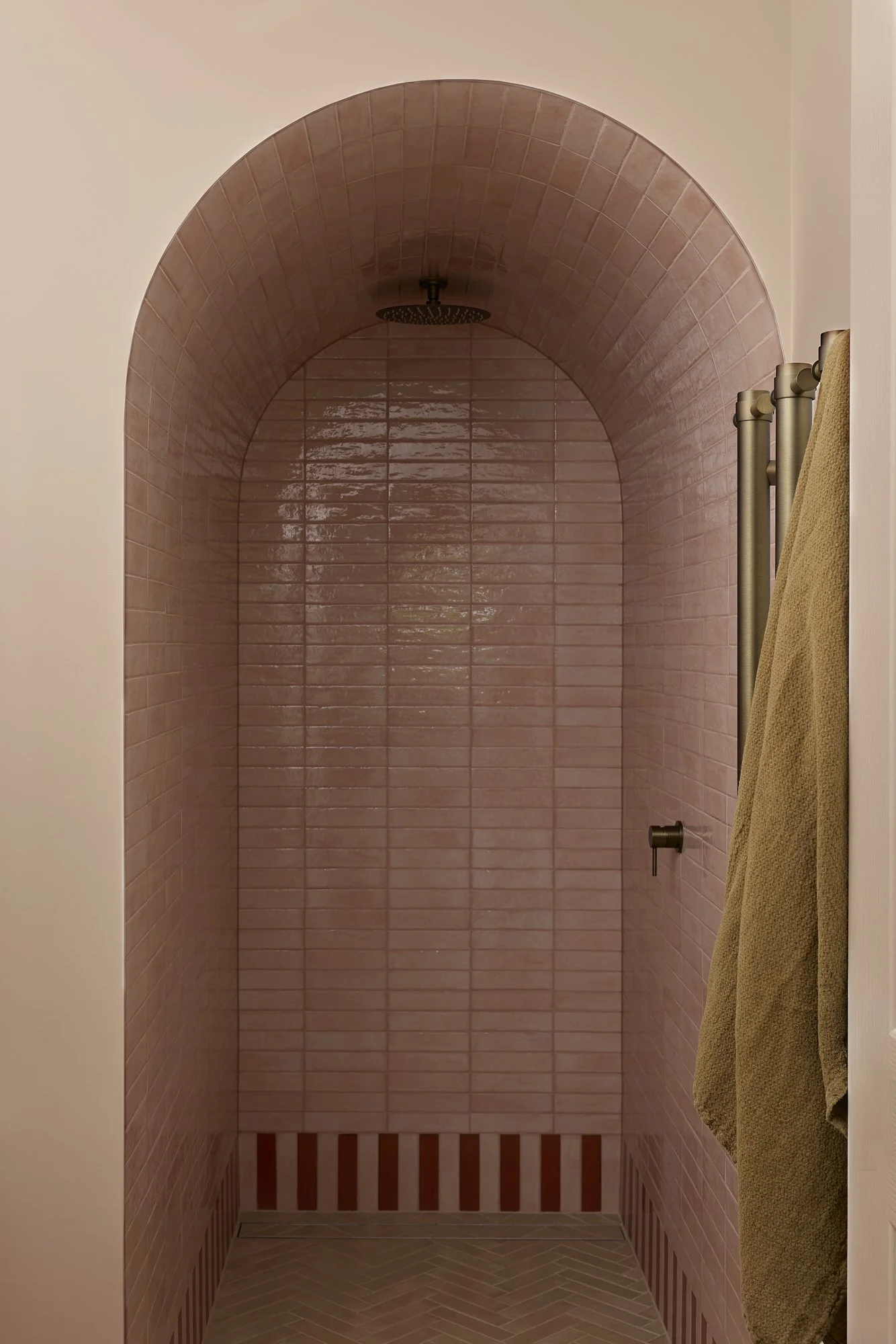 Pink arched shower lined with glossy handmade ceramic tiles, brushed brass shower fittings and patterned tiled floor in a playful contemporary Australian bathroom.
