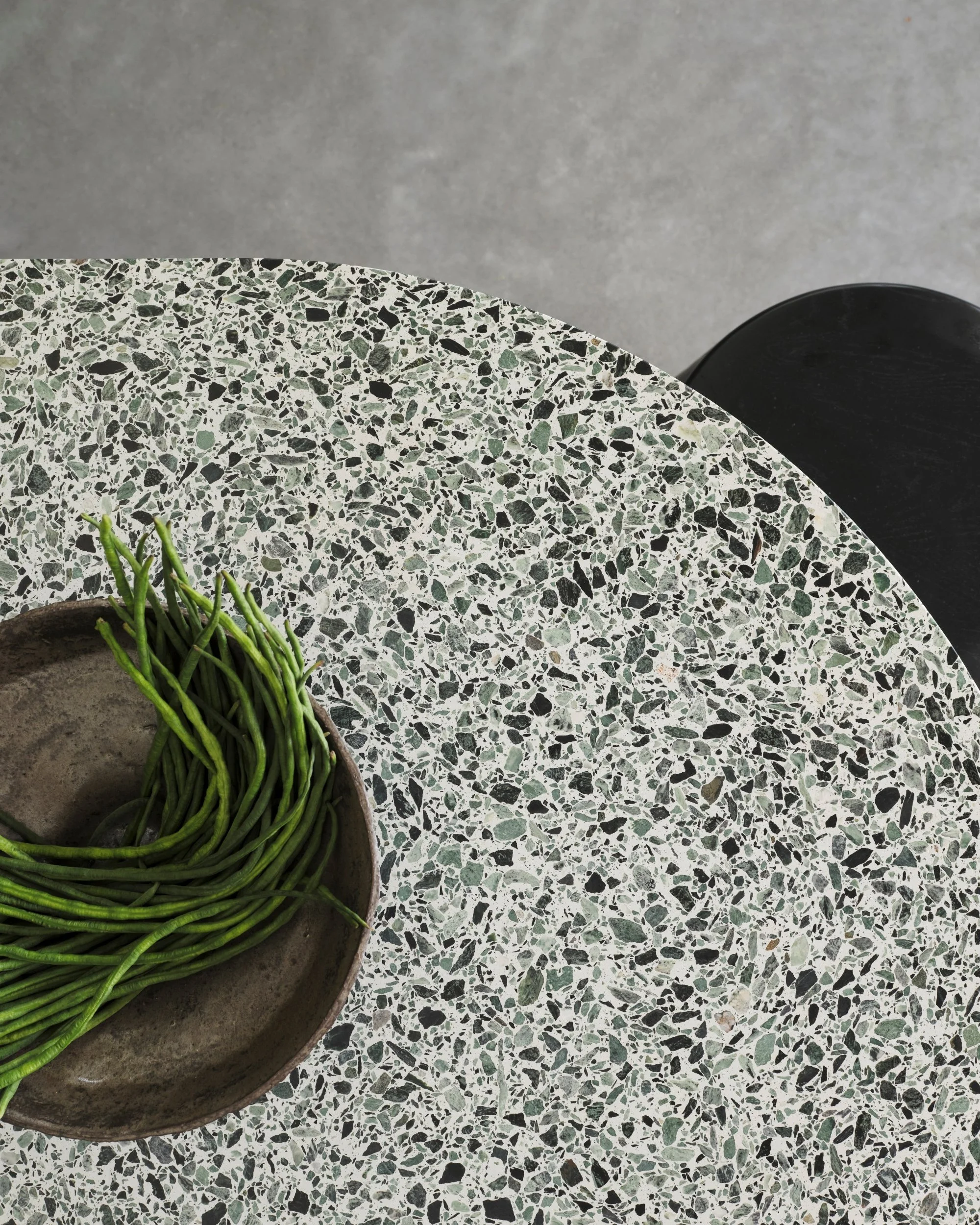 Close-up of terrazzo kitchen island with bowl of fresh greens and speckled stone surface, highlighting natural textures and modern kitchen material detailing.