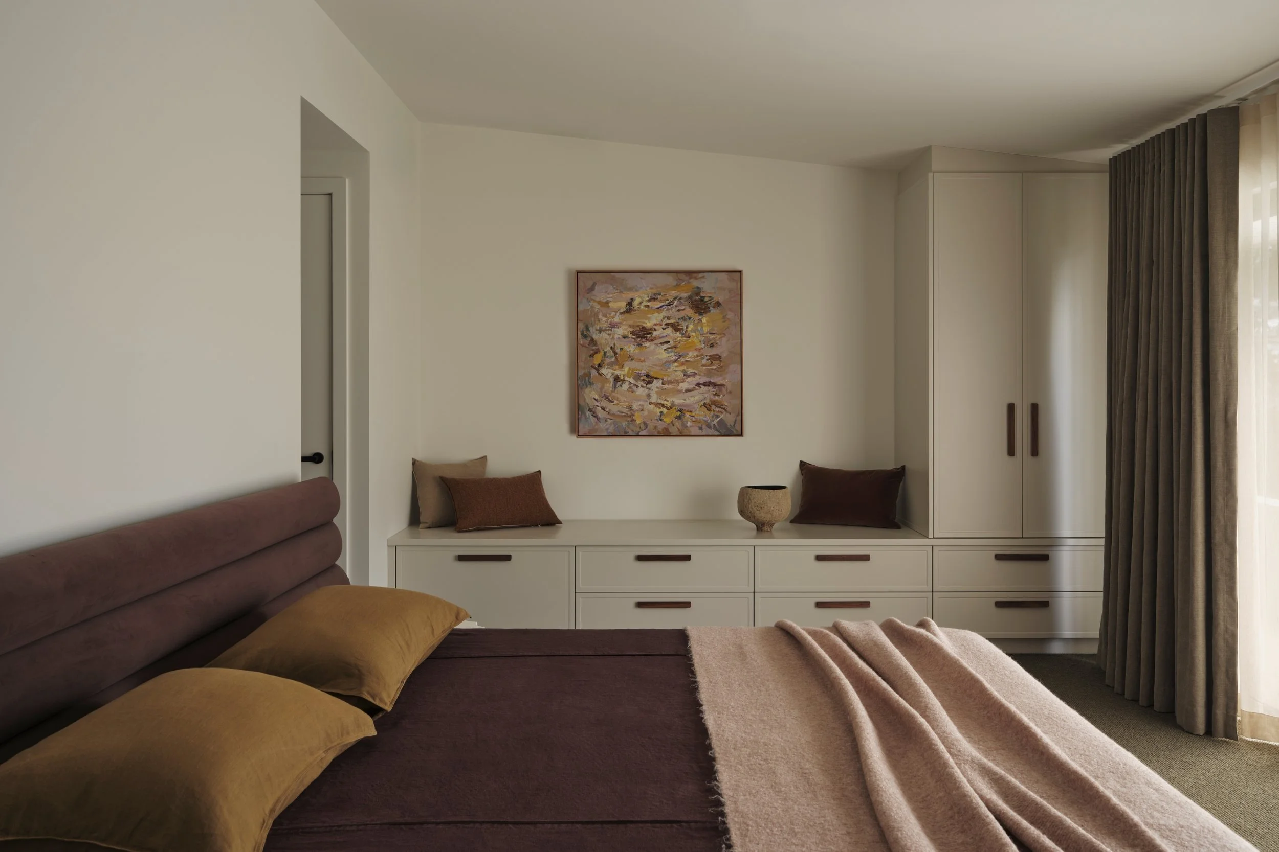 Modern bedroom with leather bed, built-in cabinetry, window seating and soft neutral palette, blending functional storage with warm interior design.