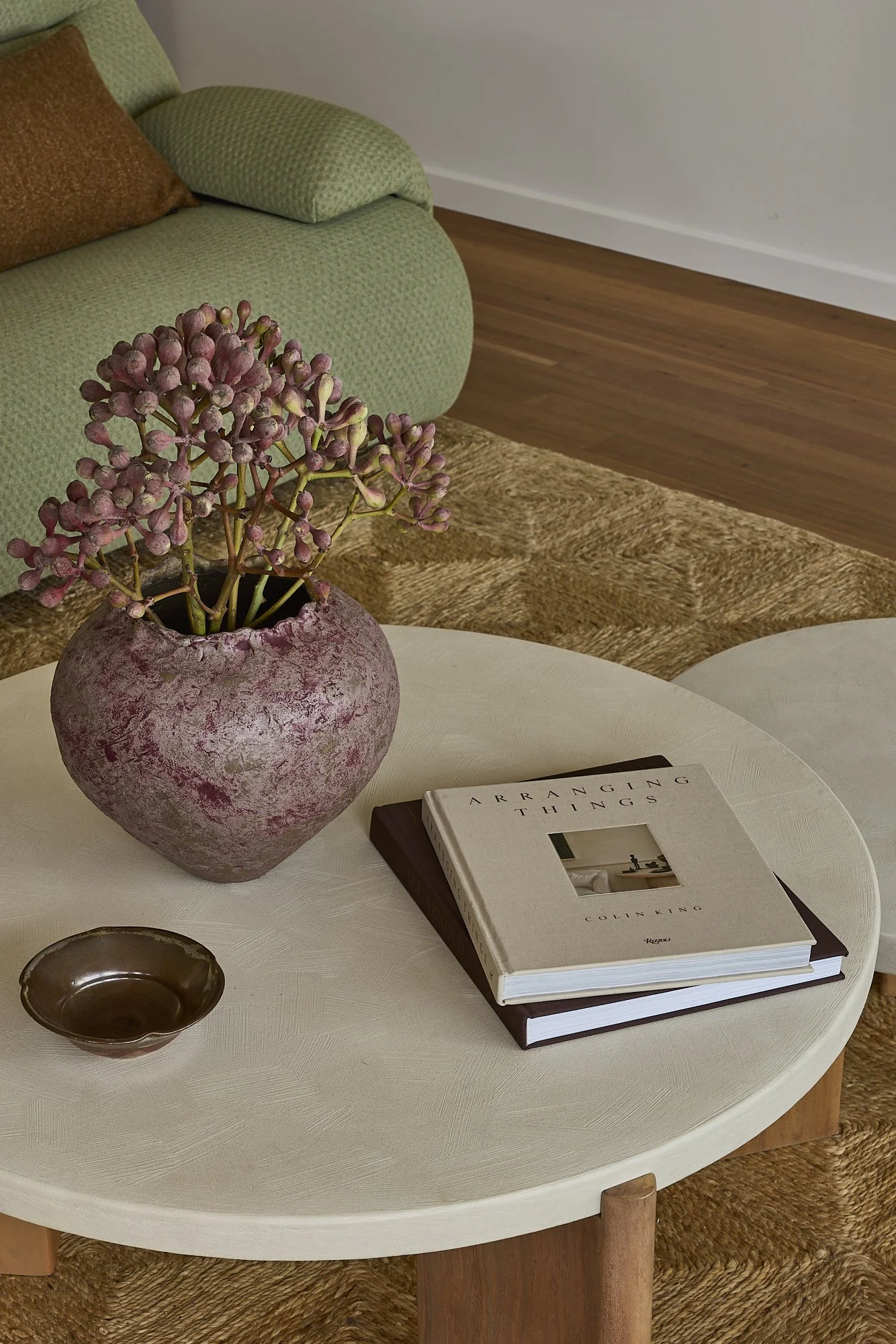 Contemporary living room featuring textured green sofa, sculptural coffee table, ceramic vase and warm timber flooring styled with natural materials in a modern Australian home.