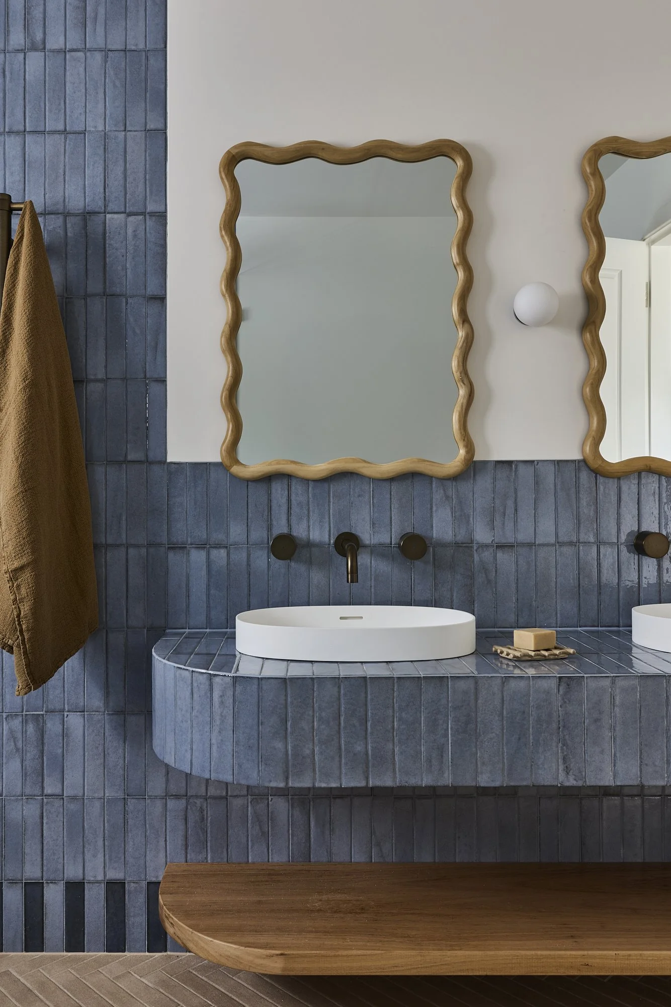 Curved blue tiled bathroom vanity with round white basin, bronze wall-mounted tapware, sculptural timber-framed mirror and bespoke timber bench in a contemporary Australian coastal home by Revel Design.
