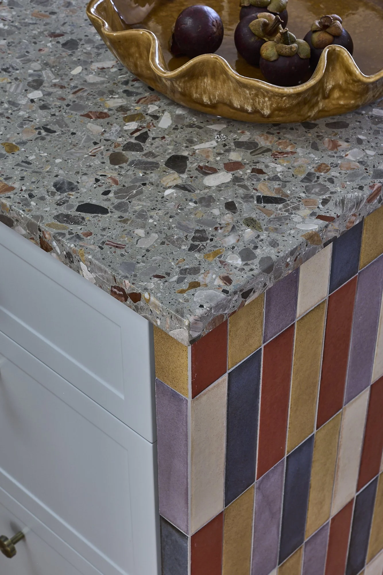 Terrazzo kitchen benchtop with handcrafted multicoloured vertical tiles and sculptural ceramic bowl showcasing bespoke joinery and premium material detailing.