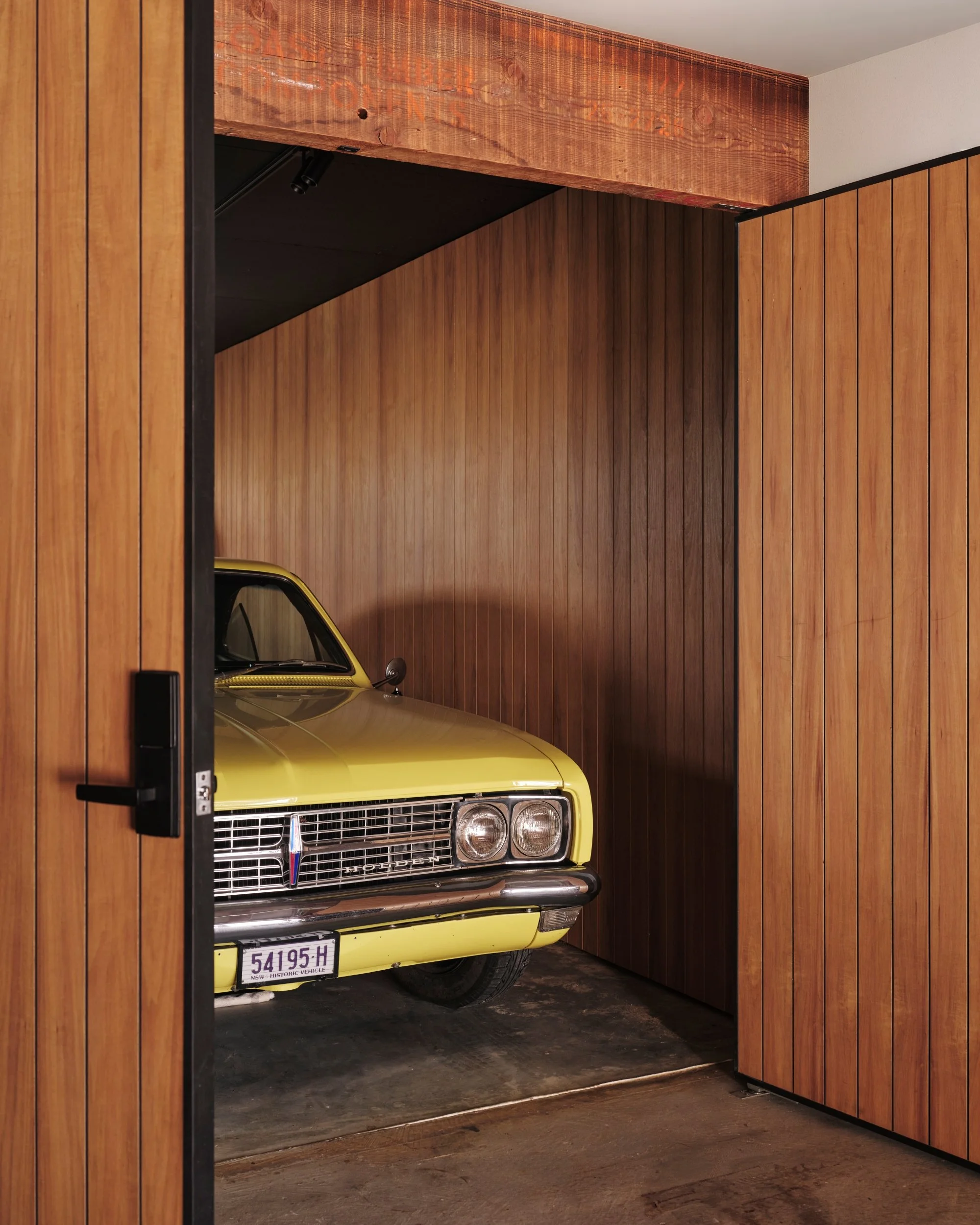 Vintage yellow Holden car parked inside a custom timber-clad garage with vertical wood panels and modern black door hardware, showcasing a contemporary residential architecture detail in Avoca.