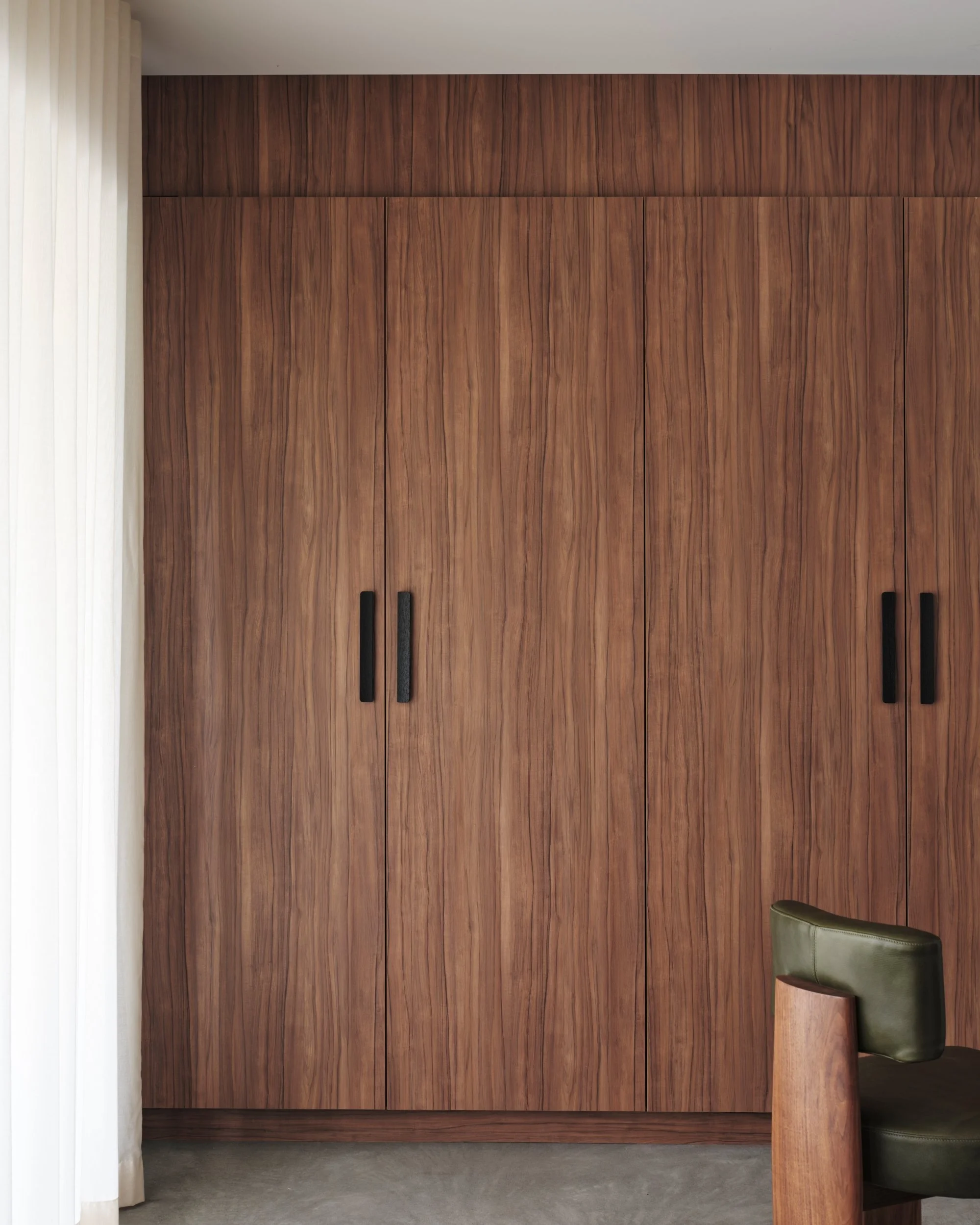 Full-height walnut cabinetry with black handles forming a concealed bar and storage wall, showcasing bespoke timber joinery in contemporary residential design.