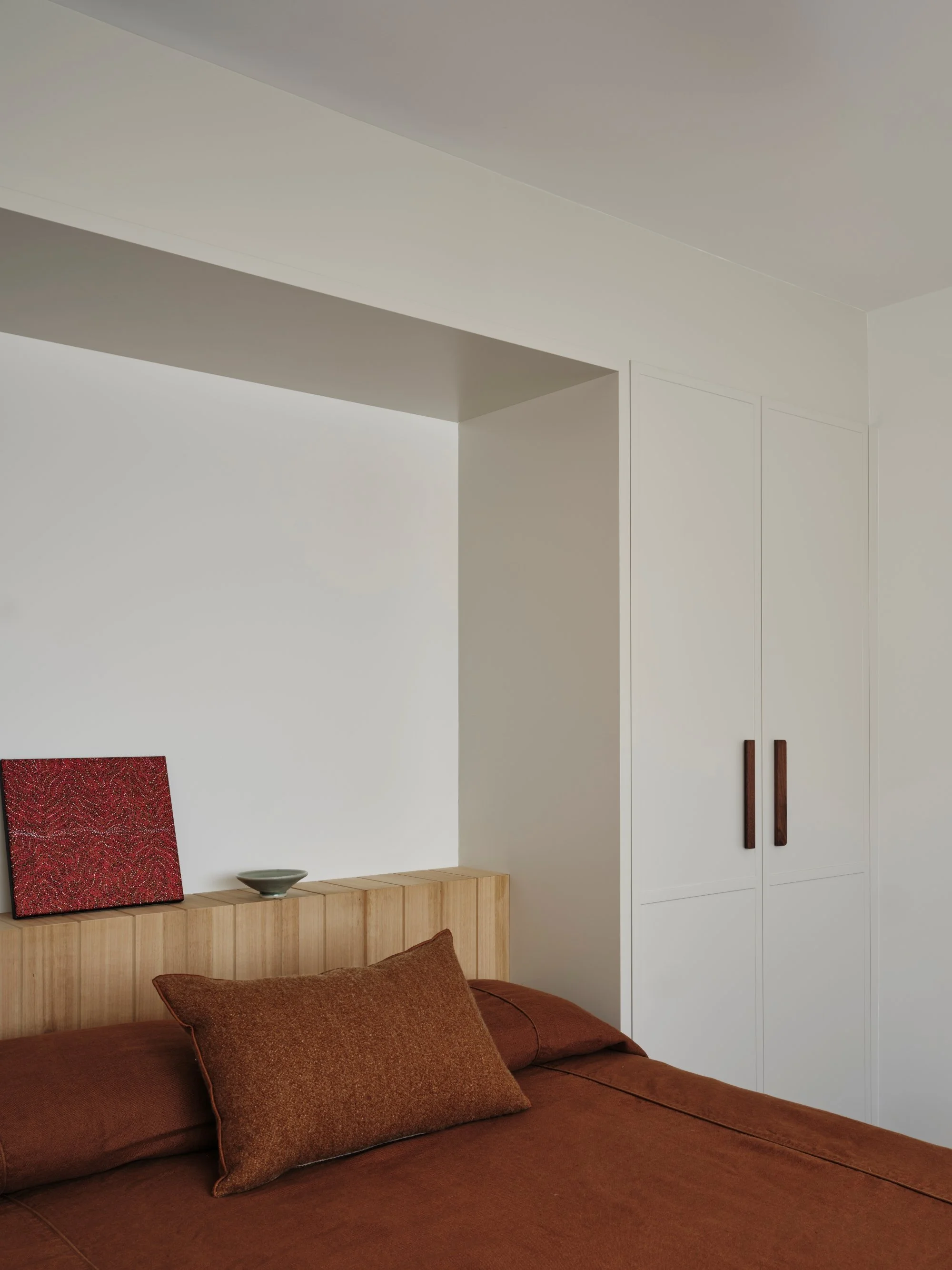 Warm-toned bedroom with leather upholstered bed, timber headboard shelf and minimalist wall art, styled with earthy textures in a calm contemporary interior.