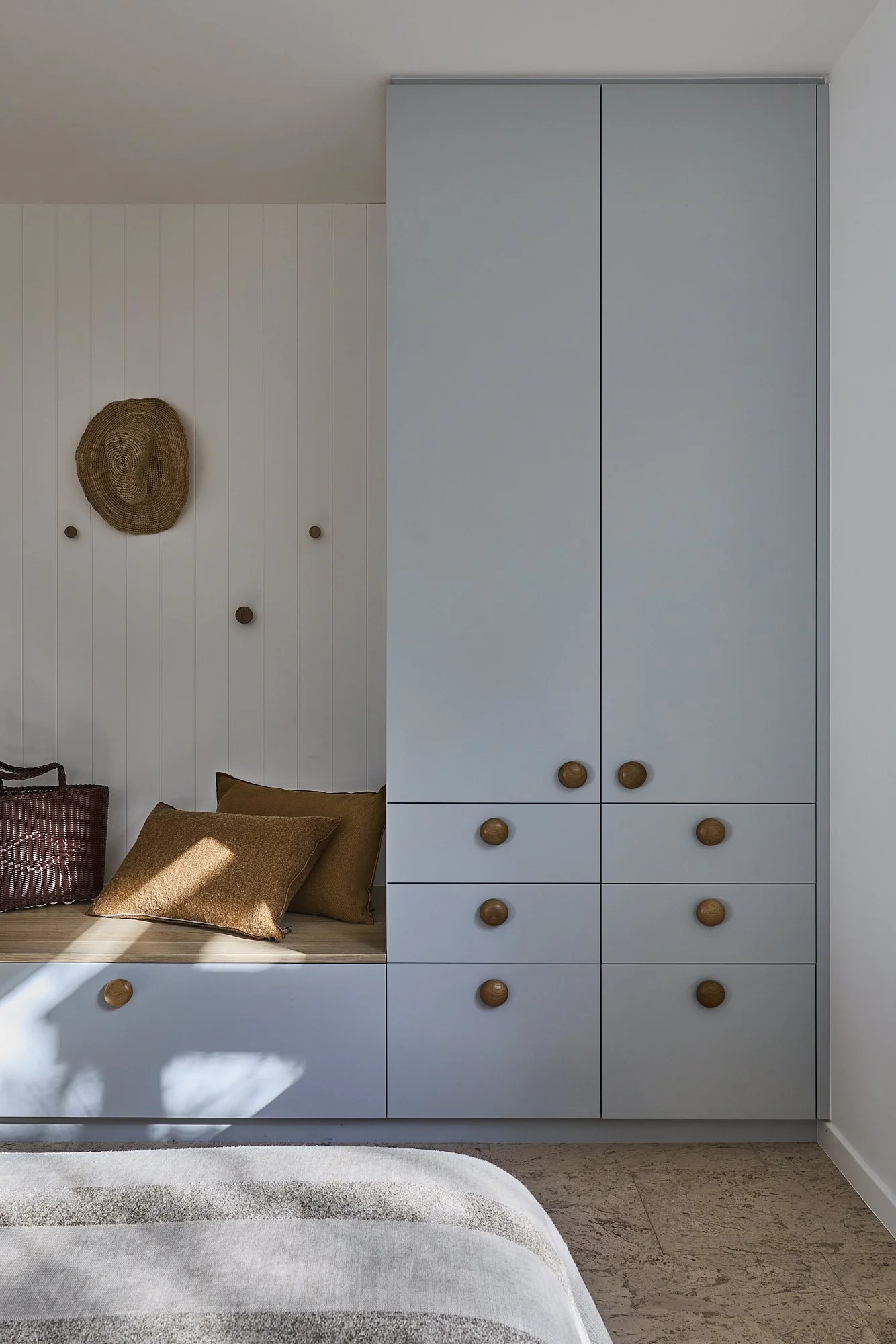 Custom bedroom joinery with soft blue wardrobes, integrated window seat, timber shelving and warm oak detailing in a contemporary Australian coastal home interior.