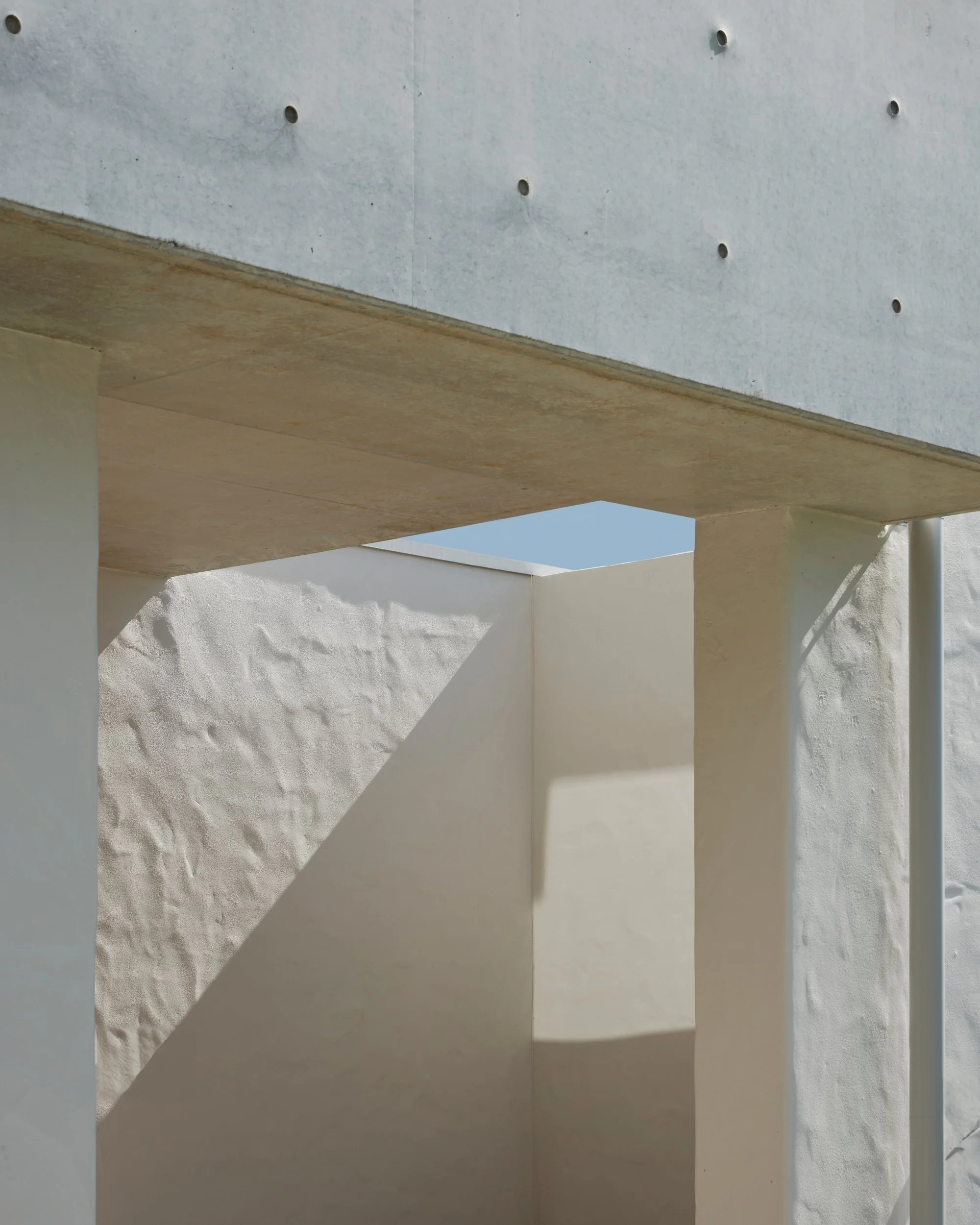 Architectural detail of textured white walls and exposed concrete balcony casting strong geometric shadows, highlighting minimalist modern home design and sculptural forms.