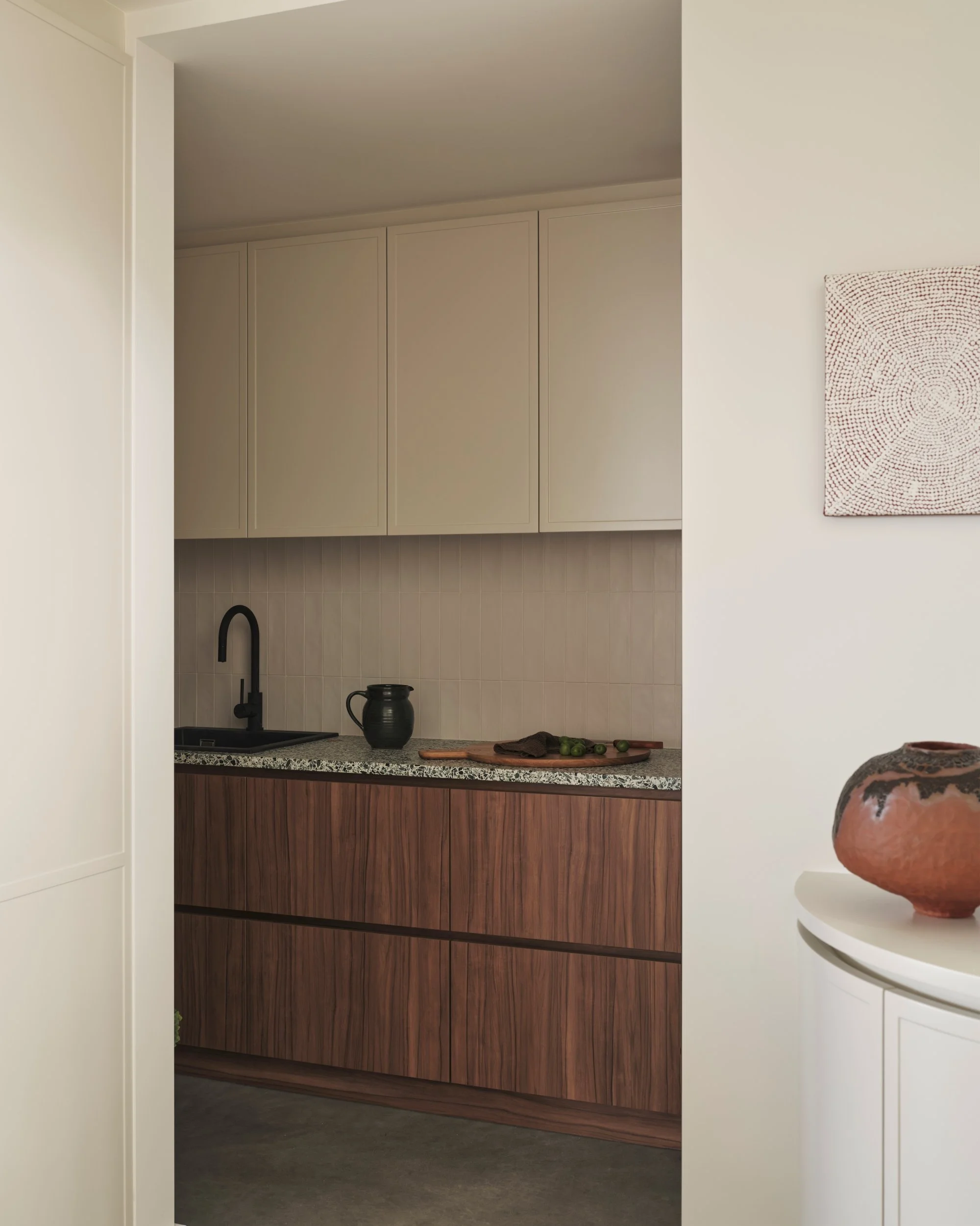 Walk-in pantry with walnut cabinetry, terrazzo benchtop, matte black tapware and light cream overhead cupboards, blending warm timber joinery with modern kitchen storage design.