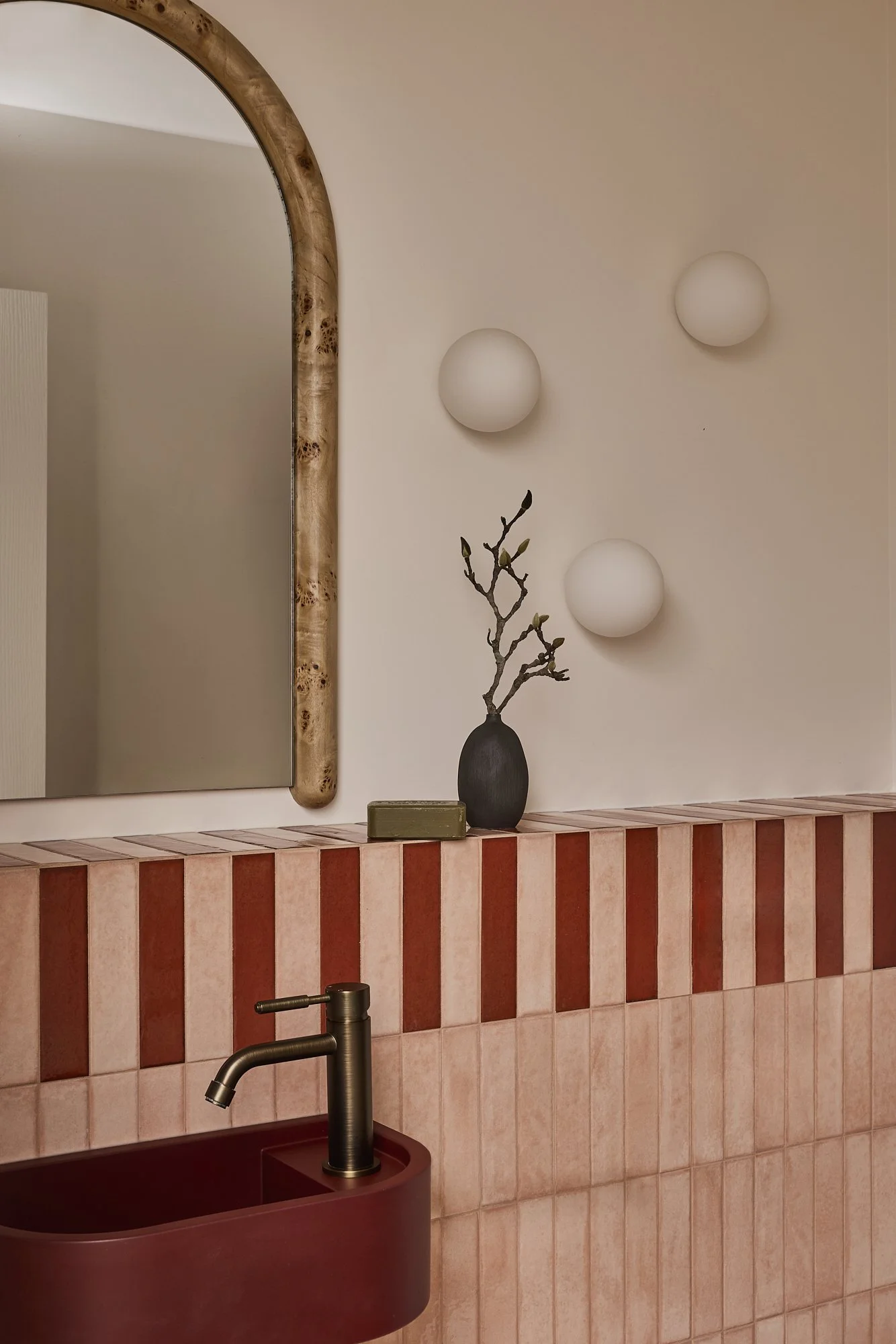 Contemporary pink bathroom with burgundy freestanding basin, striped ceramic splashback, sculptural timber-framed mirror and brushed brass tapware in a modern Australian home.