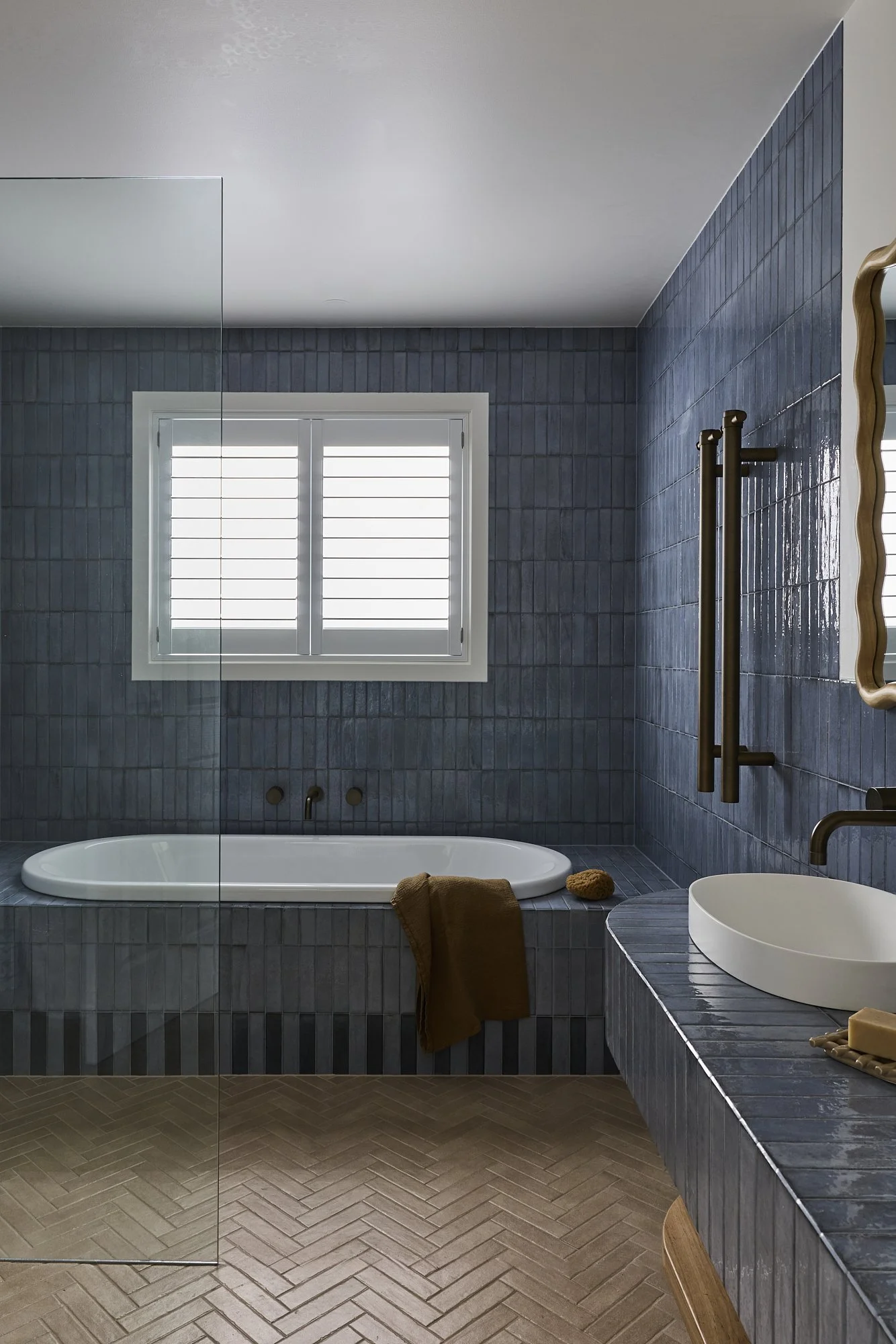 Contemporary bathroom featuring blue handmade wall tiles, freestanding bathtub, frameless glass shower, bronze tapware and timber-framed mirror in a light-filled Australian coastal home renovation.