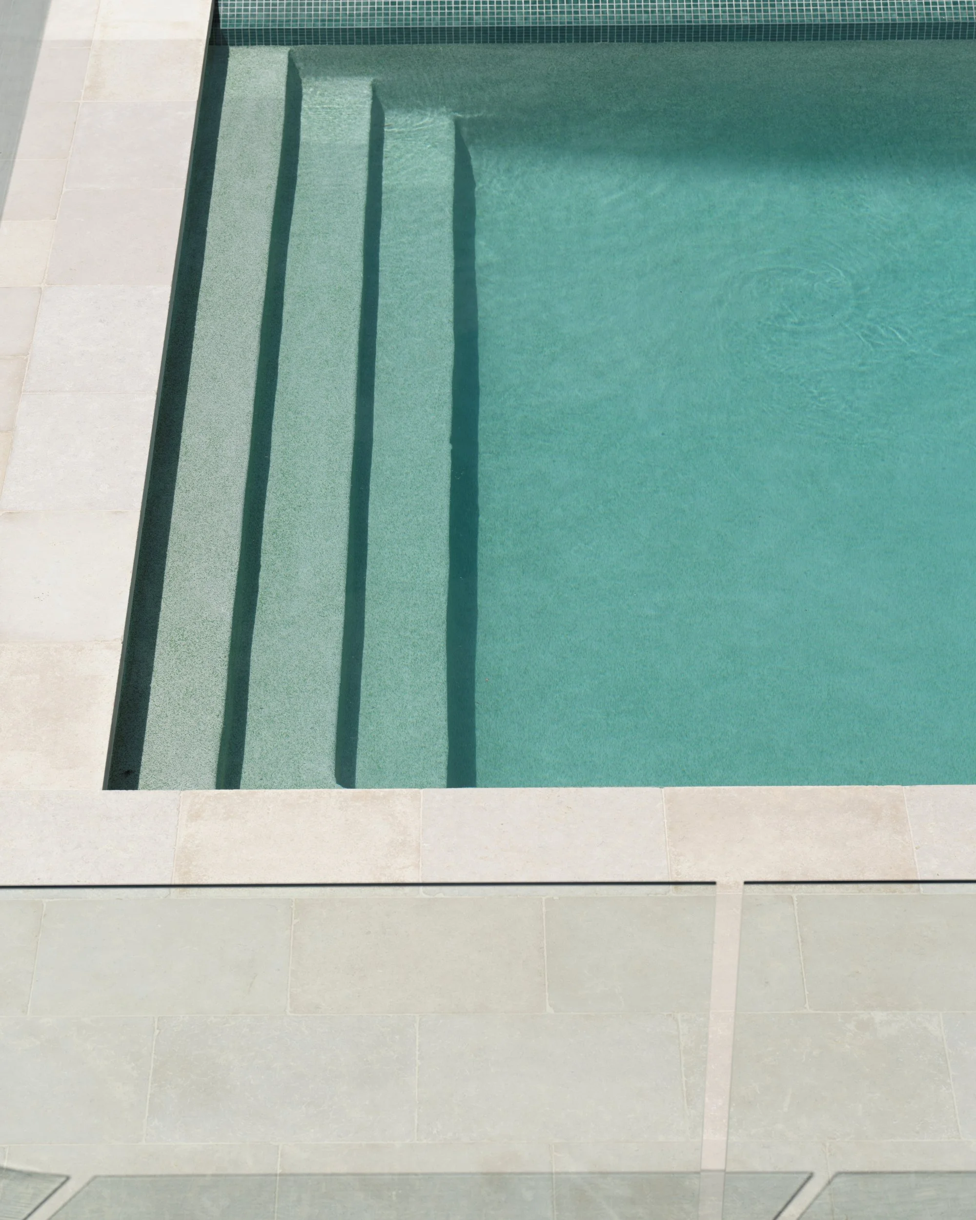 Minimalist swimming pool with wide entry steps, pale stone coping and turquoise water, highlighting clean geometric lines and contemporary outdoor design.
