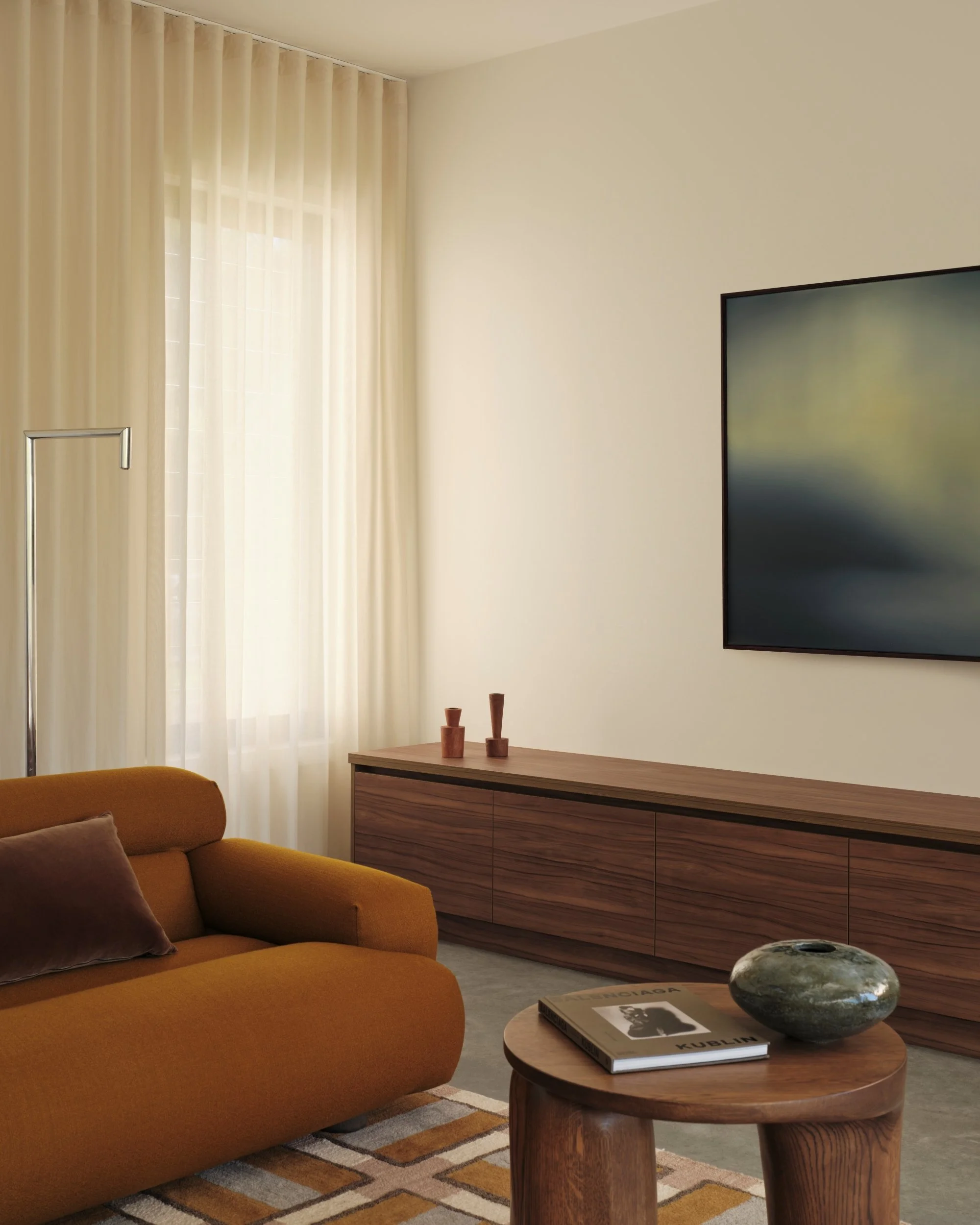 Contemporary living room corner with rust-toned sofa, timber sideboard and abstract artwork, styled with minimalist decor and sheer curtains filtering natural light.