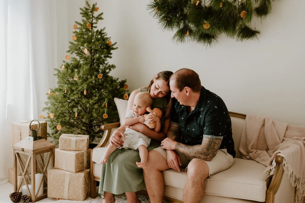 A christmas photo by Coop & Co Creative. A woman, man, and their toddler enjoy themselves in an indoor photography studio, styled for Christmas.