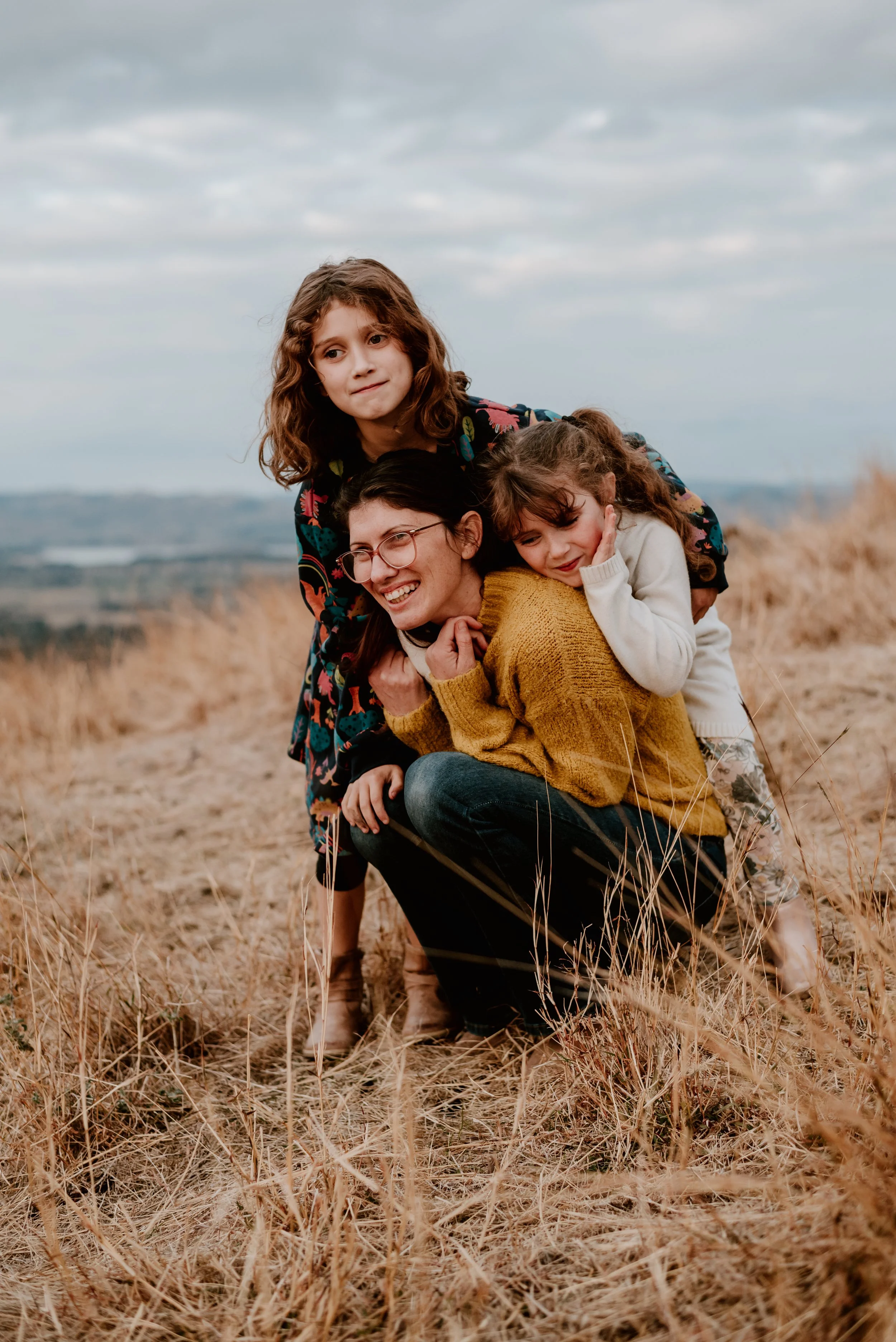 A woman with three young girls on Huon Fill in a field of tall grass, smiling and enjoying a playful moment. Albury-Wodonga Family photography by Coop & Co Creative
