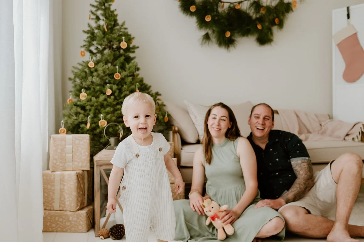 A christmas photo by Coop & Co Creative. A woman, man, and their toddler enjoy themselves in an indoor photography studio, styled for Christmas.