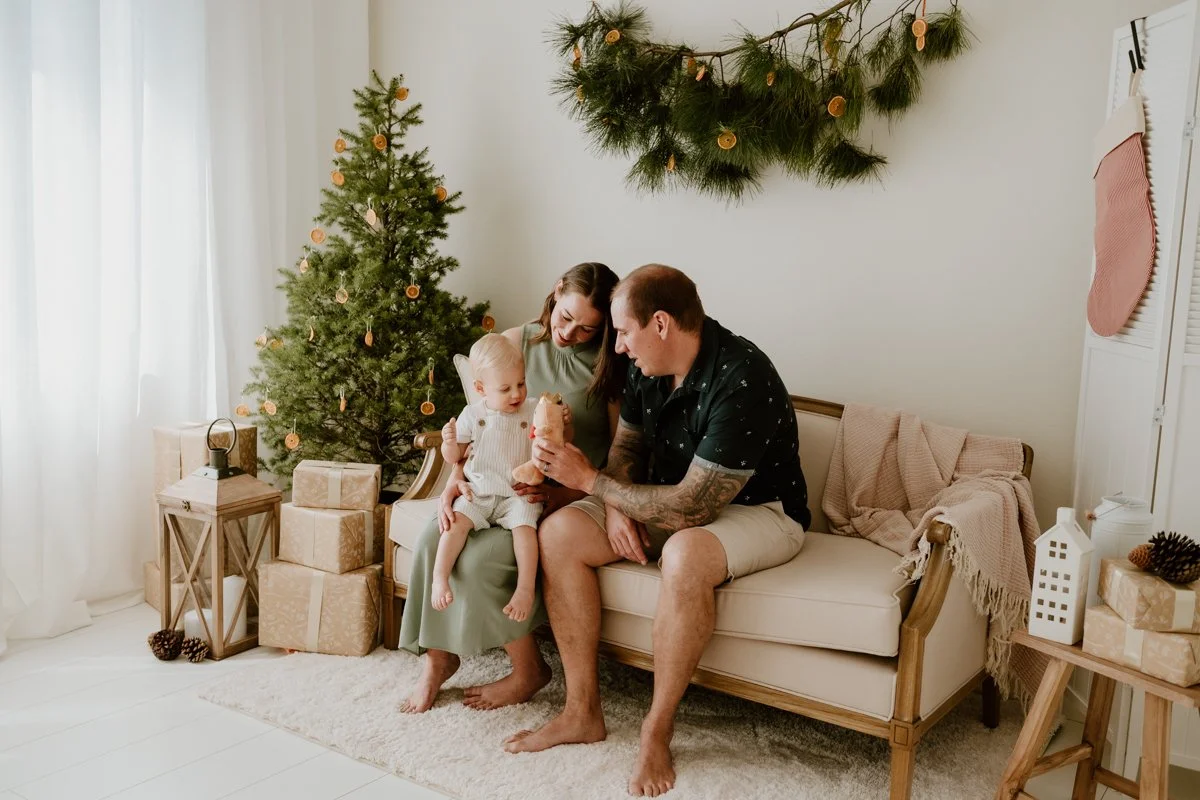 A christmas photo by Coop & Co Creative. A woman, man, and their toddler enjoy themselves in an indoor photography studio, styled for Christmas.