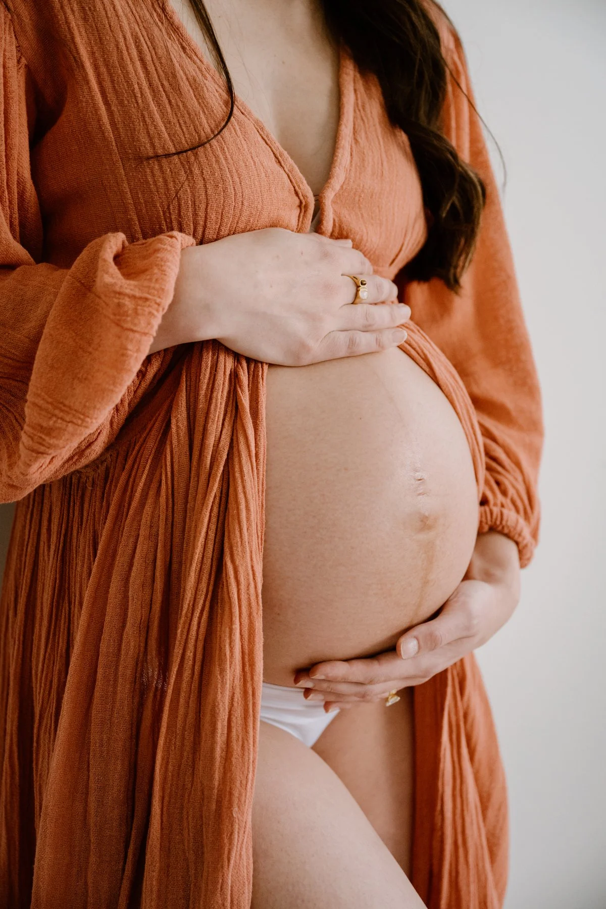 Pregnant woman in an orange dress holding her belly with both hands.