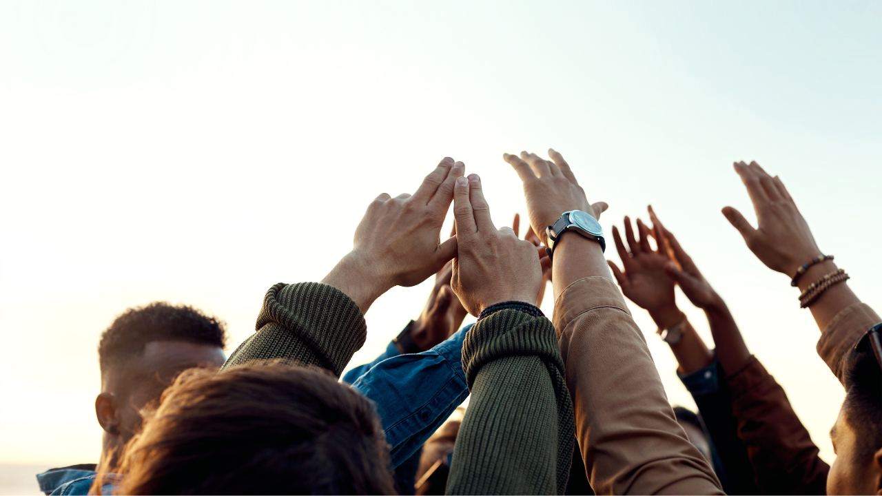 Group of diverse people outdoors raising their hands together during sunset.