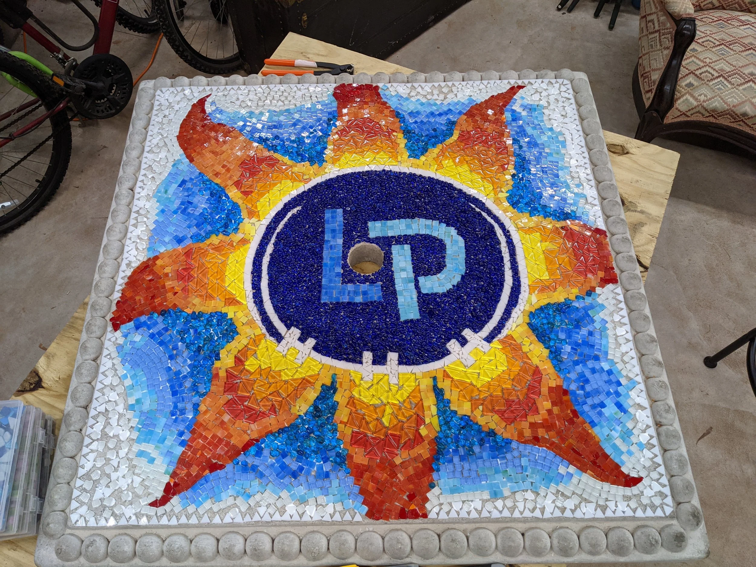 Mosaic of logo for Loew and Patel orthodontics sealed in resin on a stone table.