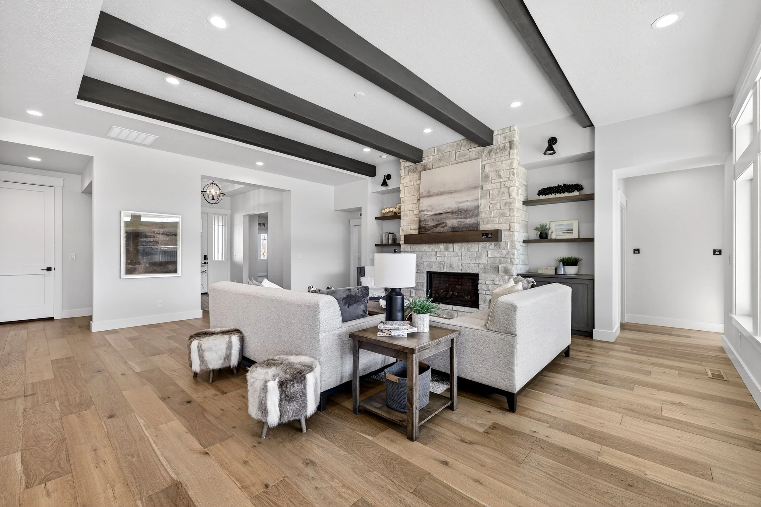 Modern living room with white walls, wooden floor, gray couches, a stone fireplace, and built-in shelves with decor.
