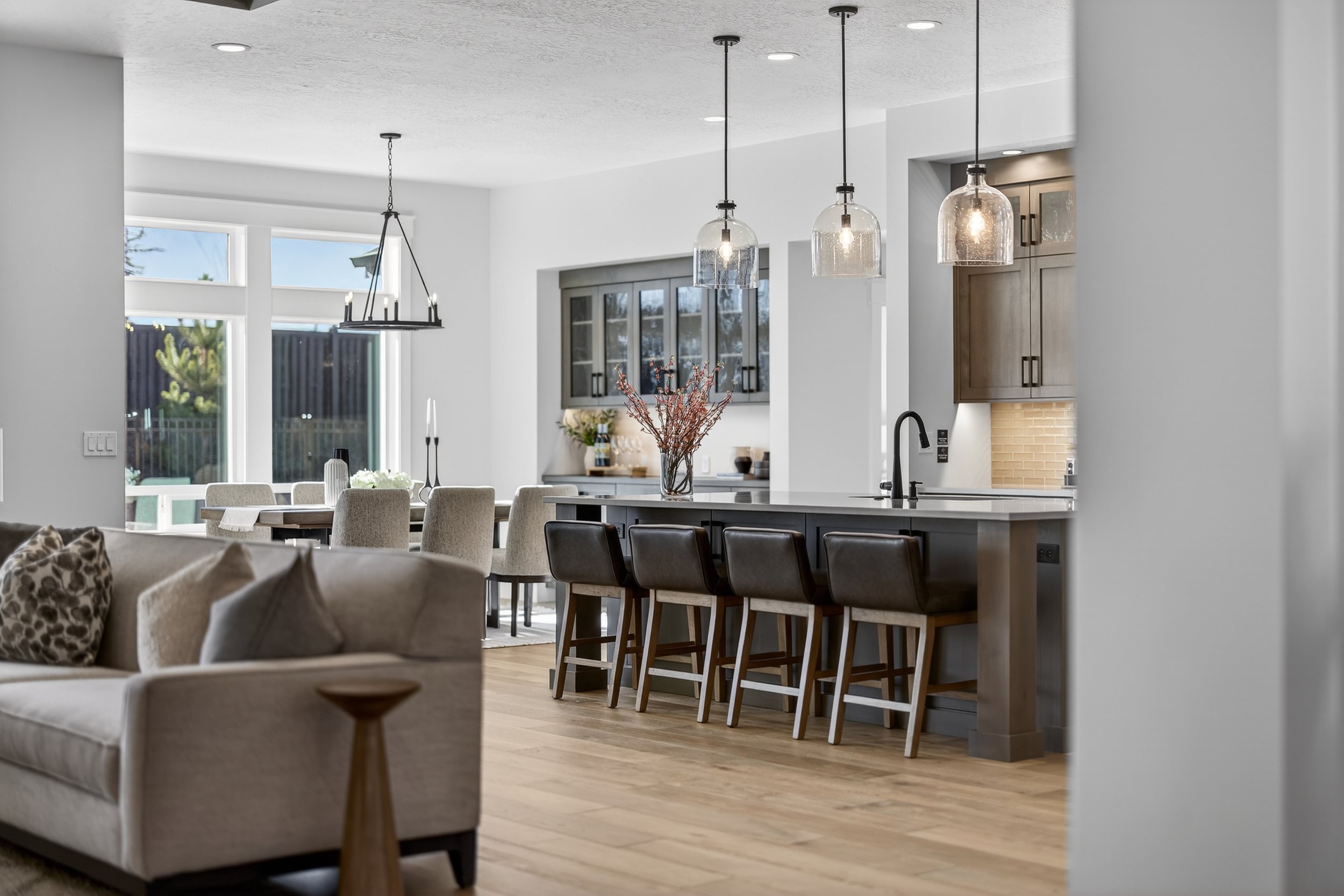 Modern open-concept living space with a kitchen featuring an island with bar stools, pendant lights, a dining area with chairs, and a living area with a sofa.