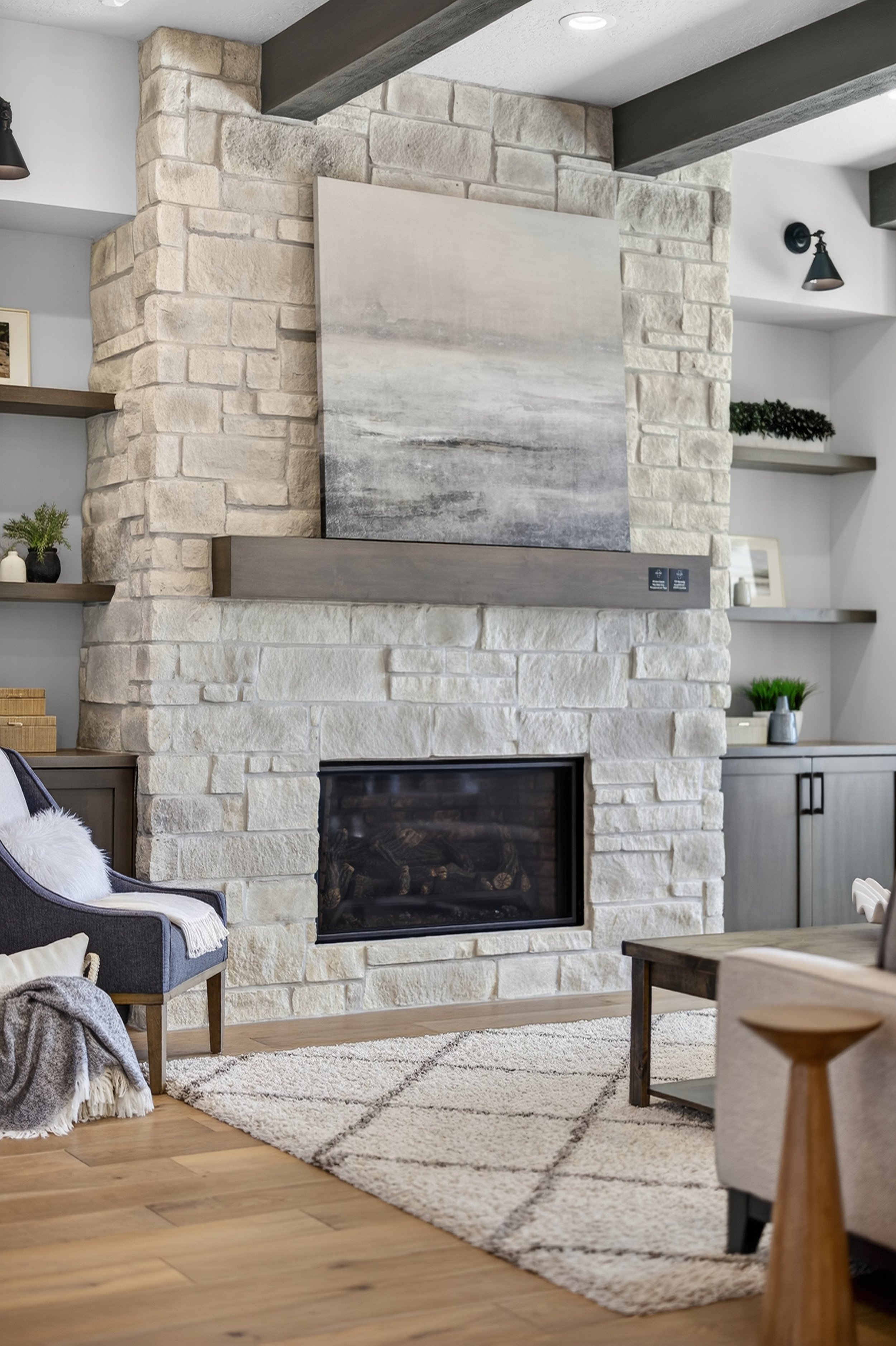 Living room with a stone fireplace, mounted painting, and built-in shelves with decor plants and picture frames.