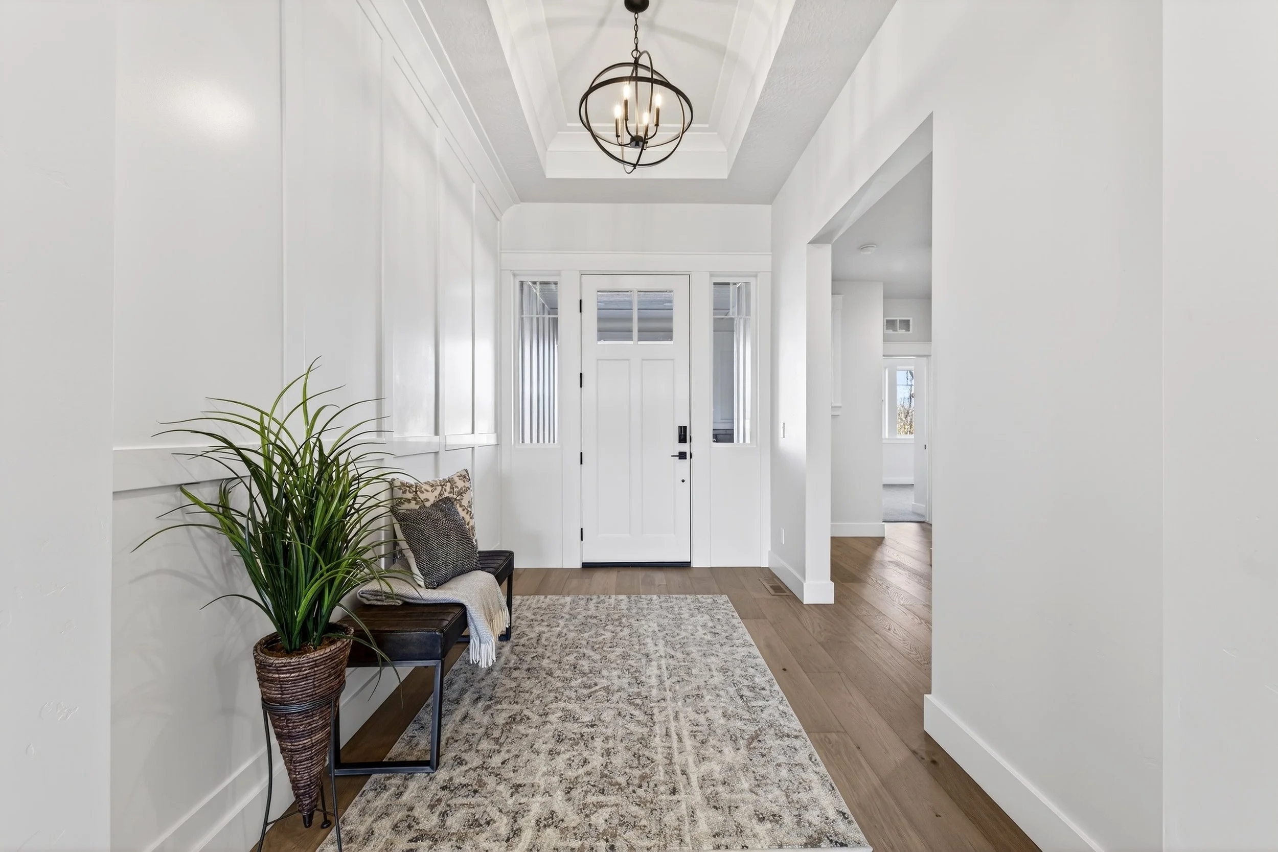 Bright entryway with white walls, a front door, a plant, a bench with pillows and a blanket, and a chandelier