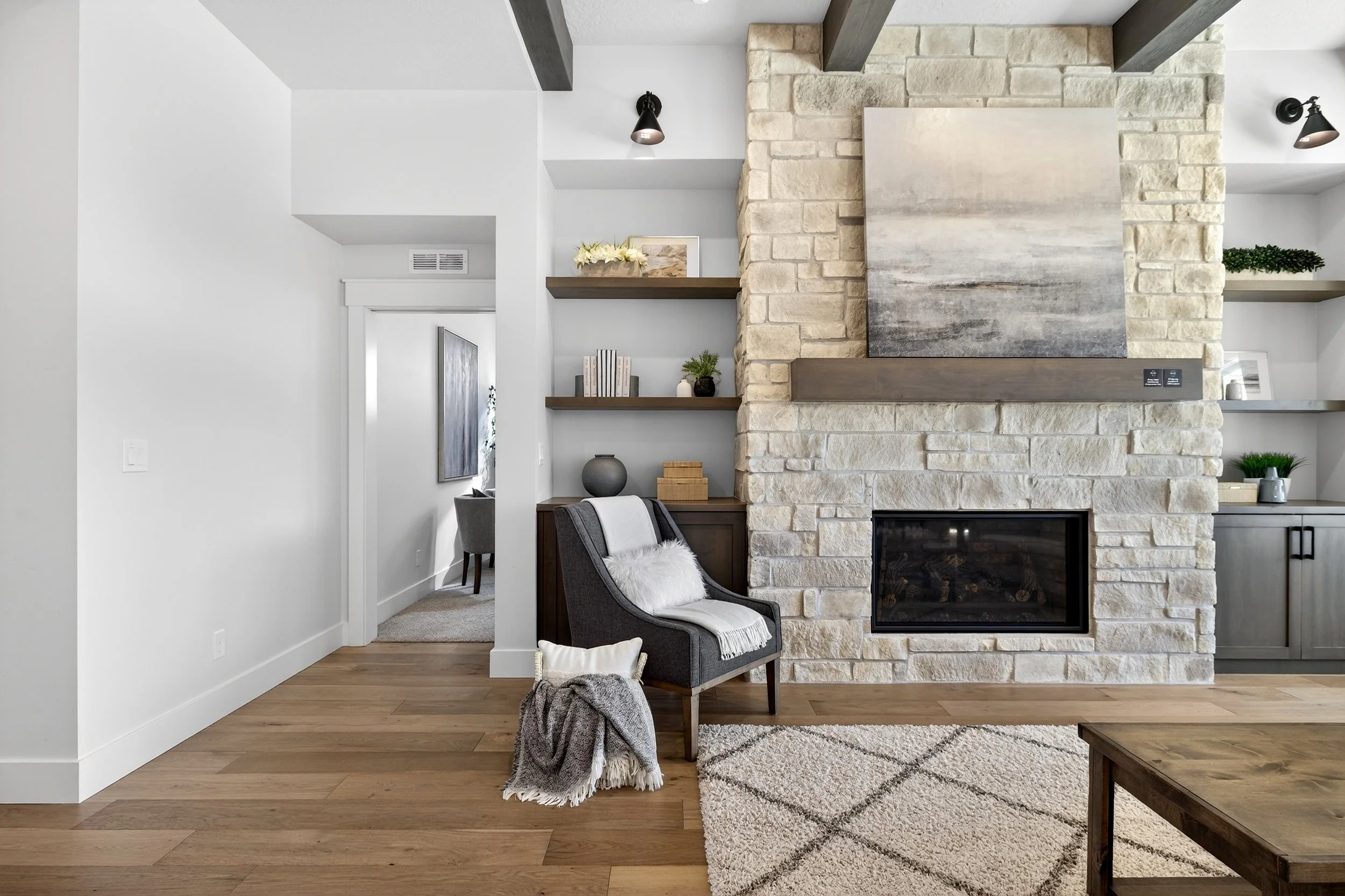 Living room with stone fireplace, gray armchair, beige rug, and built-in shelves with decor.