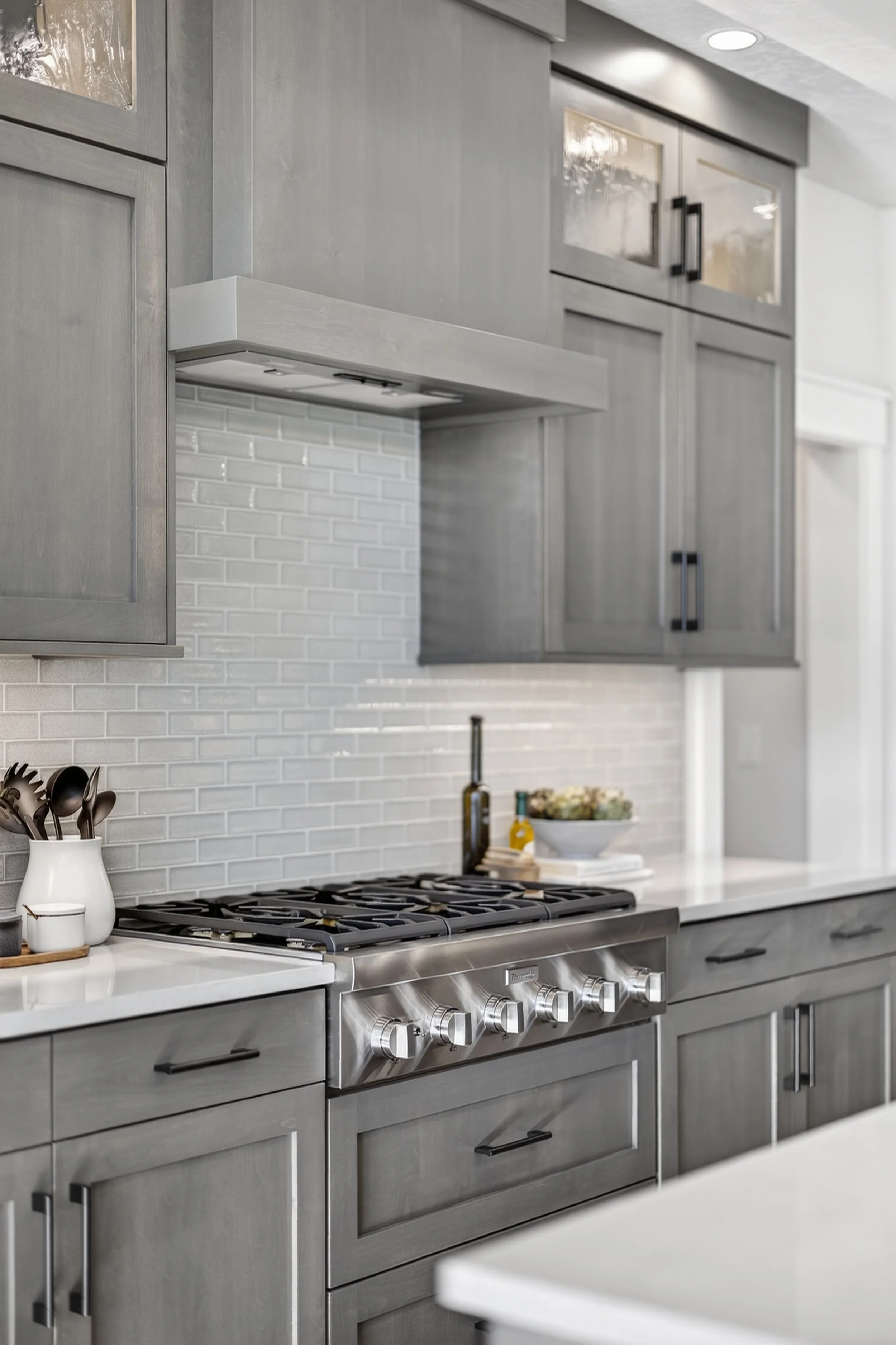 Modern kitchen with gray cabinets, white quartz counters, stainless steel stove, and white subway tile backsplash.