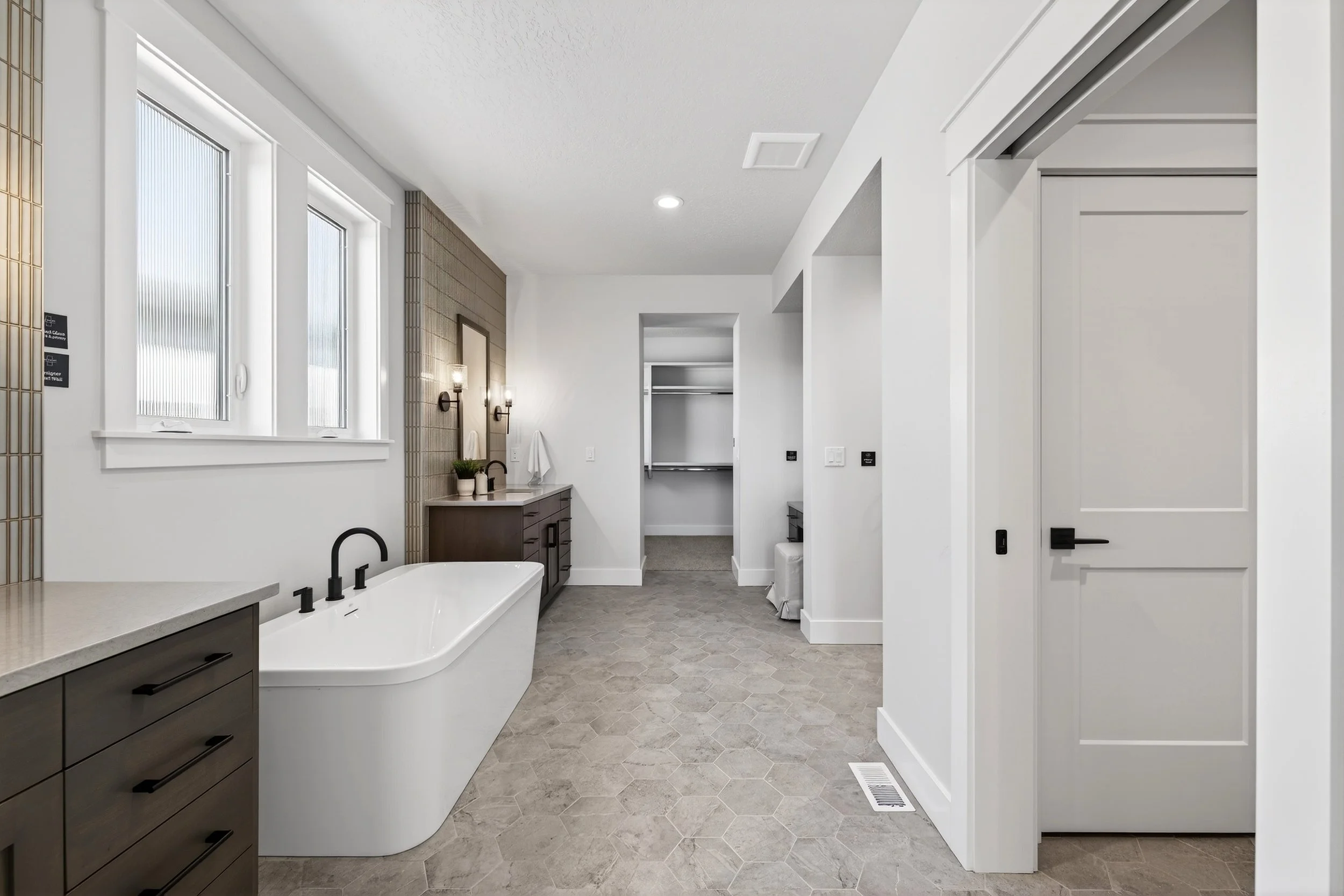 Modern bathroom with a freestanding bathtub, brown vanity, large windows, and walk-in closet in the background.