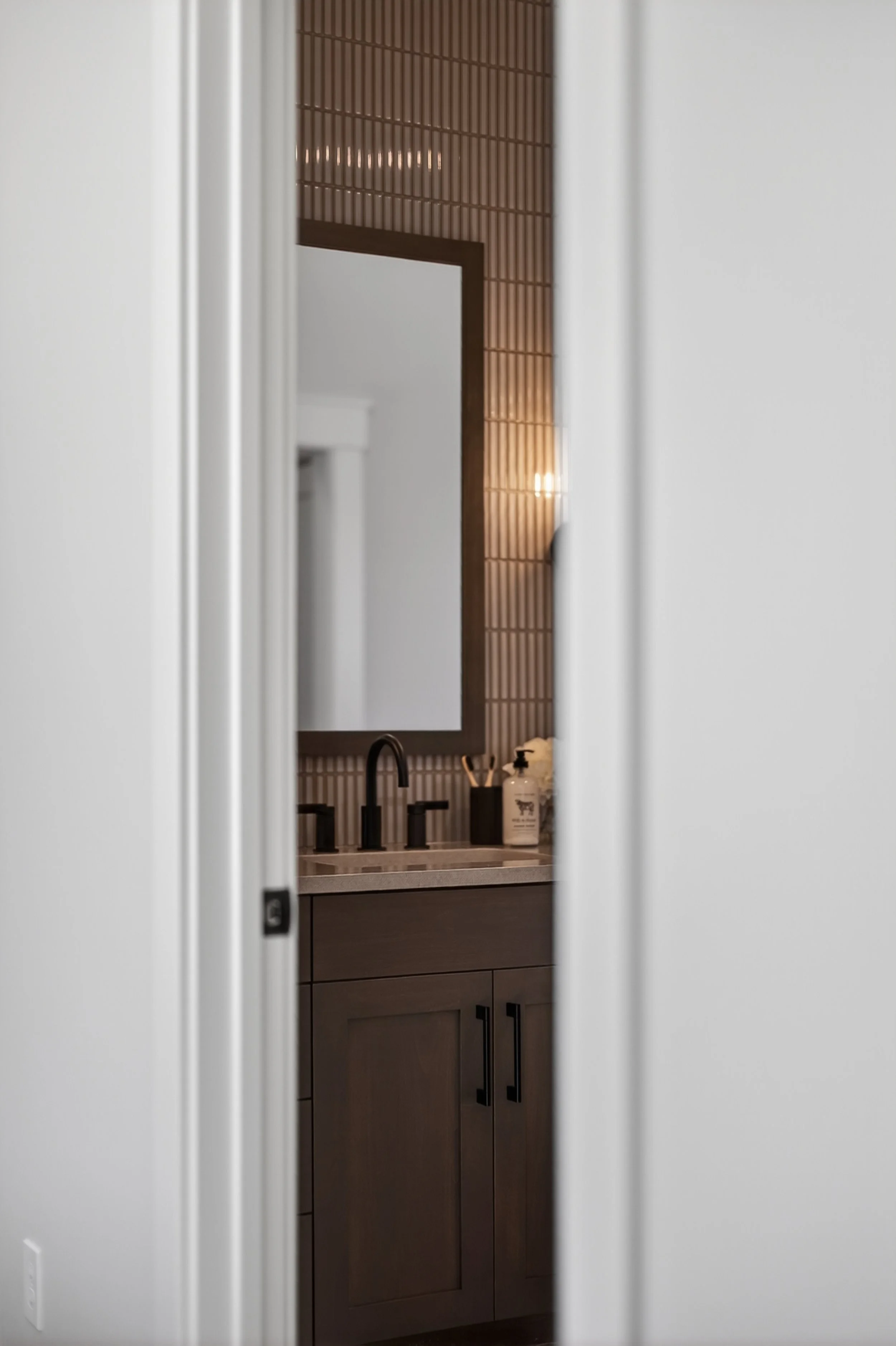 Bathroom sink area with a gray cabinet, black faucet, and mirror, seen through a partially open white door.
