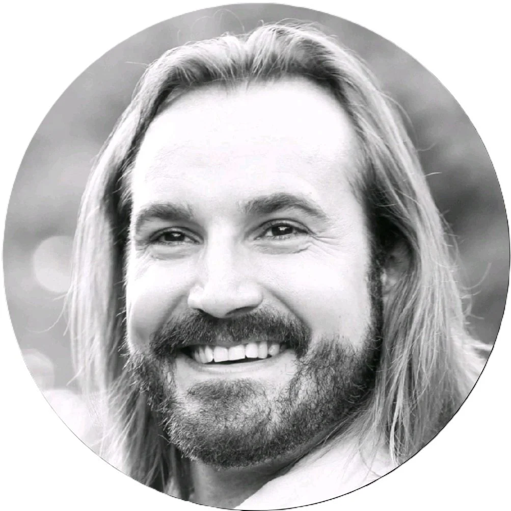 Black and white portrait of a smiling man with long hair and a beard.