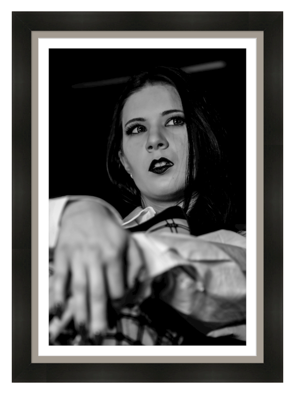 Black and white portrait of a woman with dark lipstick and eye makeup, lying on a bed with her head resting on her arm, looking off to the side.