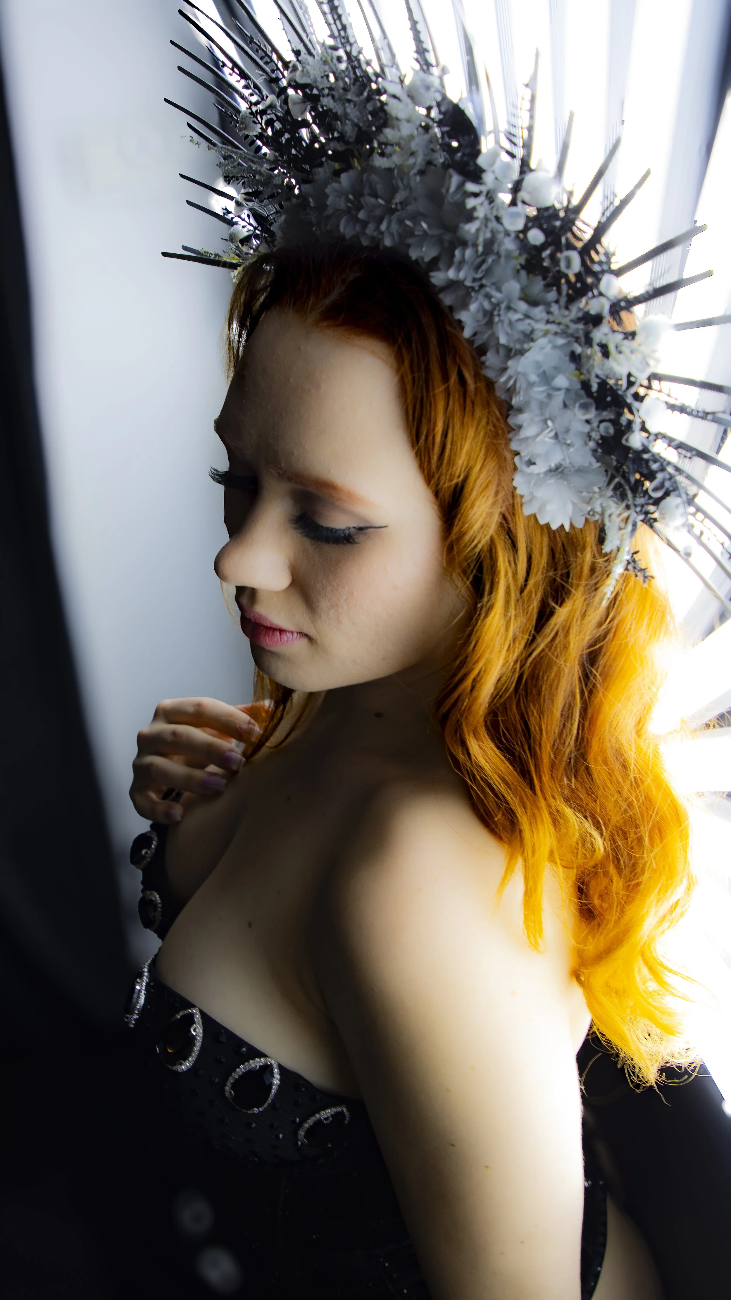 A woman with red hair, wearing a floral crown, is looking down in profile with closed eyes.