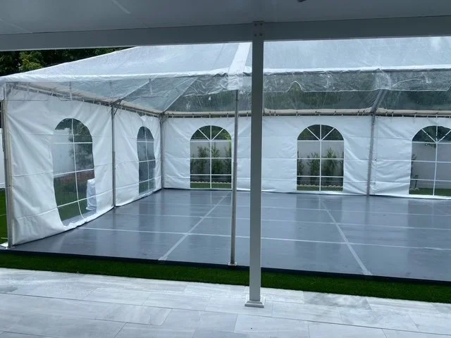 Empty outdoor event tent with clear side windows and a gray floor, seen from inside.