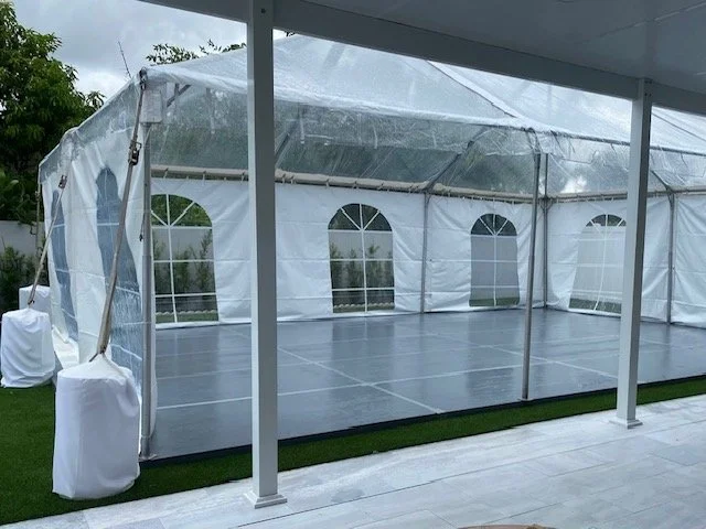 Empty outdoor event tent with transparent plastic sides and vinyl flooring, set up on grass.