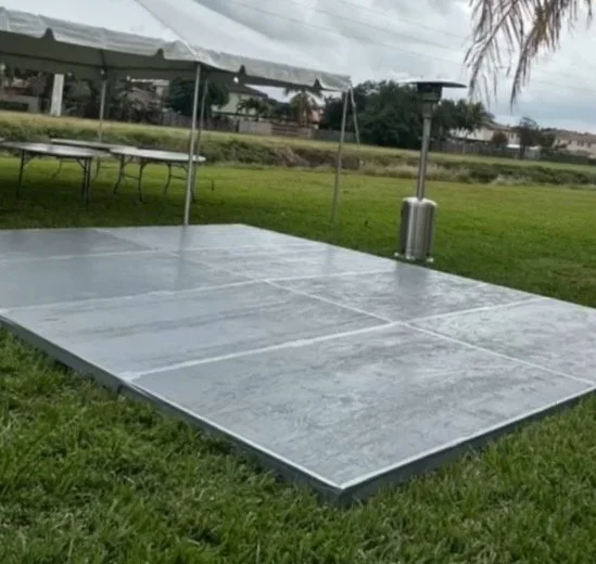 Empty outdoor stage with a tent, tables, and a propane heater on a grassy field.