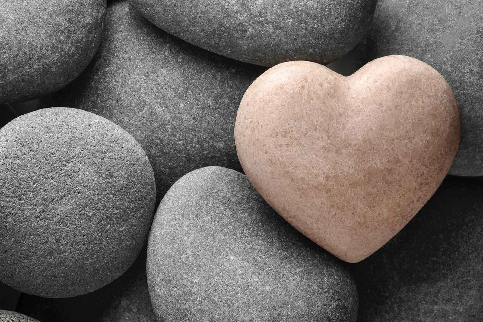 A group of smooth, rounded gray stones surrounding a pinkish-brown stone shaped like a heart.