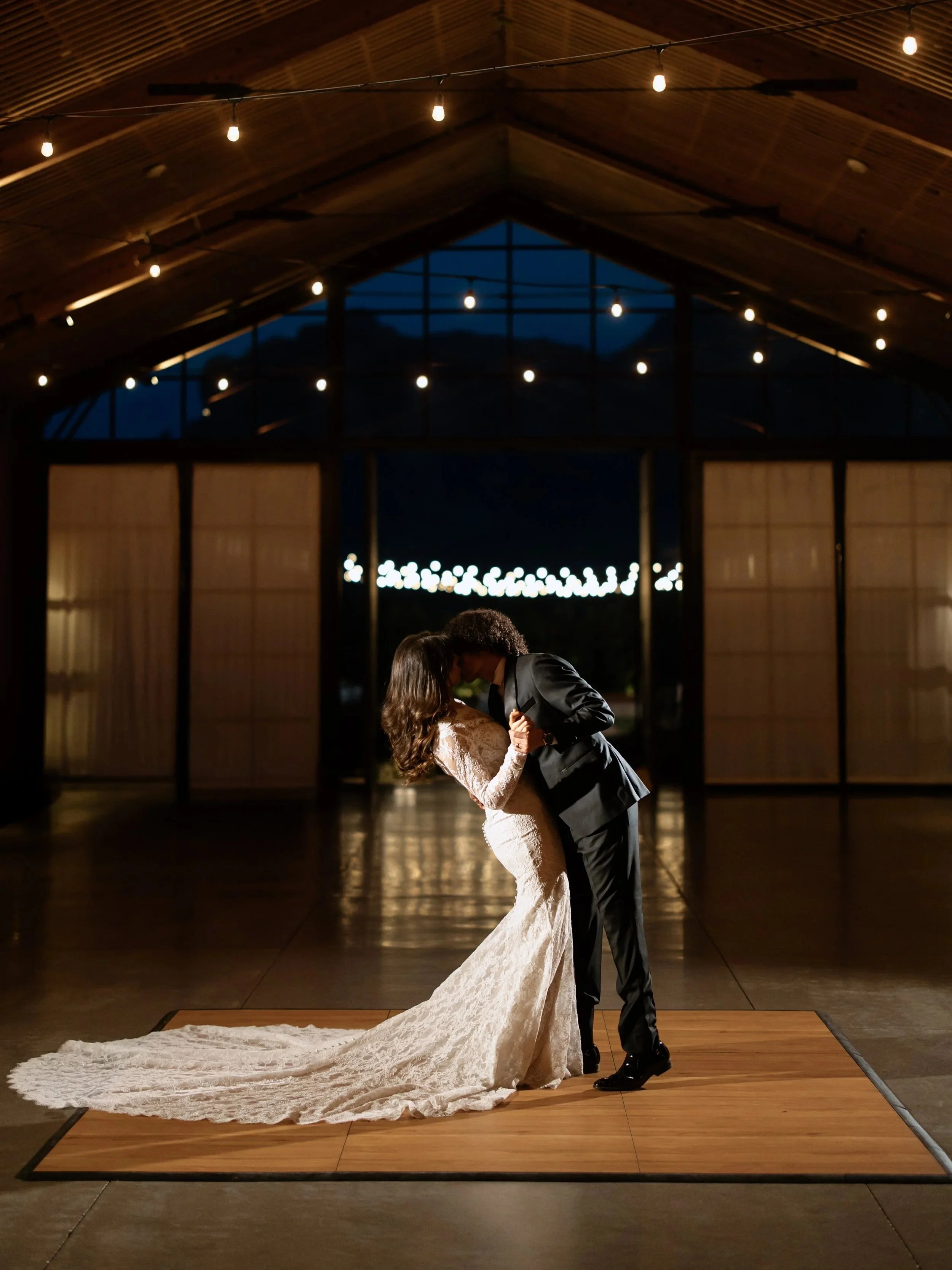 A bride and groom dancing at their wedding reception in a decorated tent with guests watching.