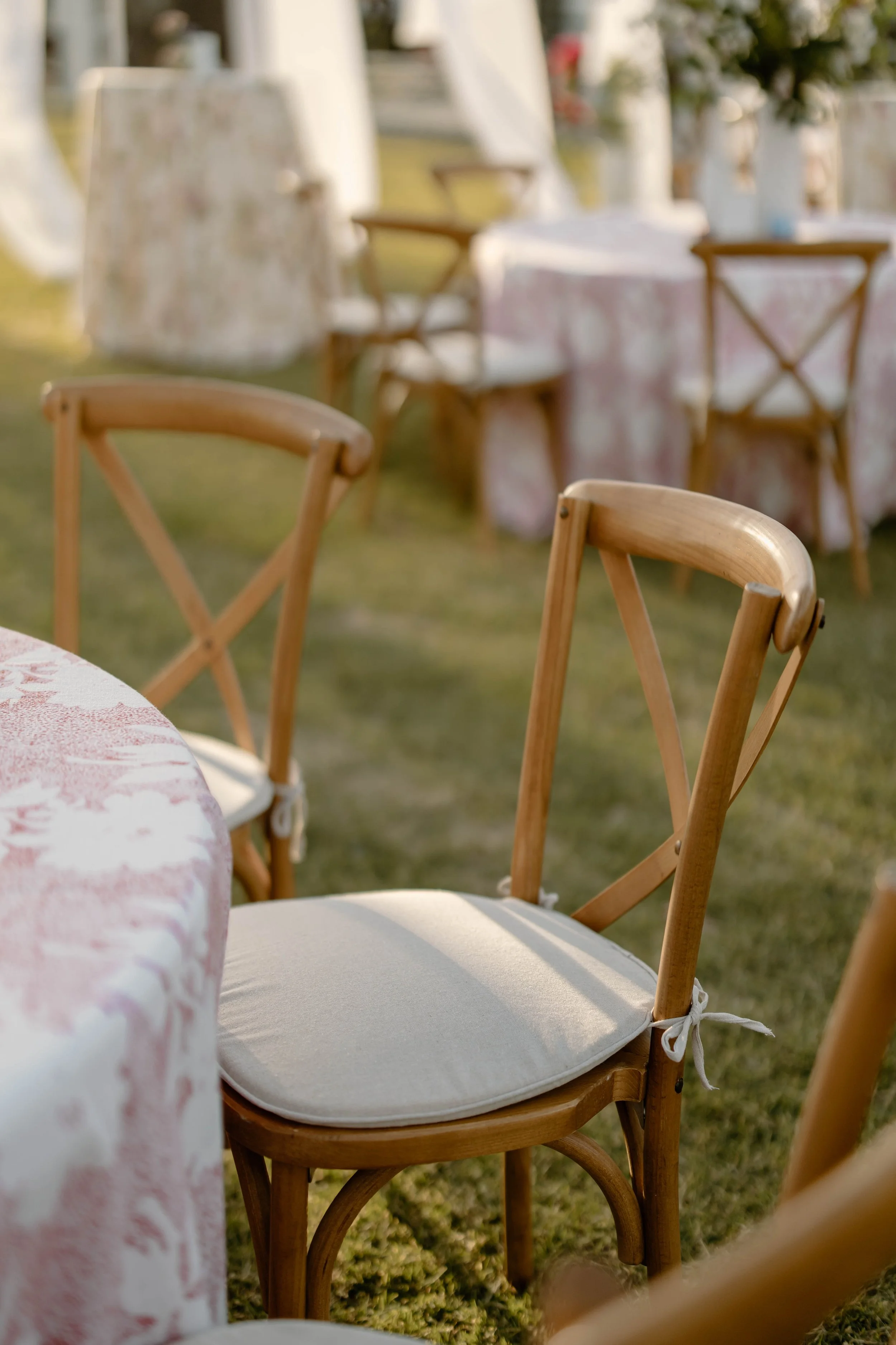 Wooden chairs around tables with floral tablecloths at an outdoor event garden.
