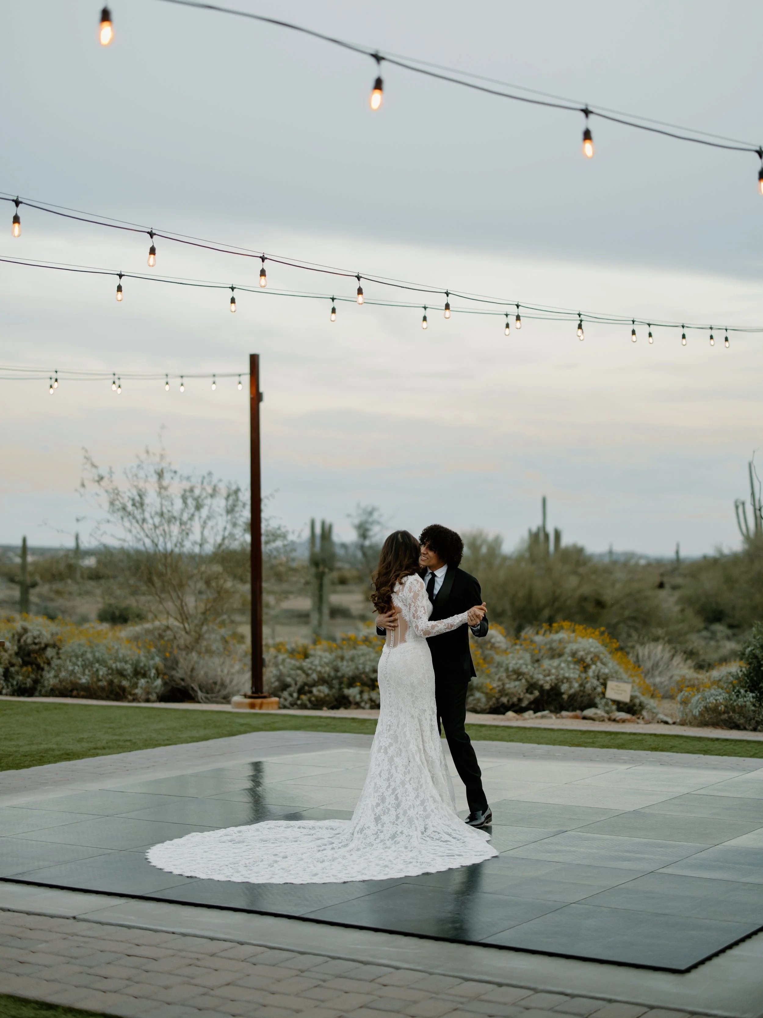 A bride and groom sharing a first dance outdoors during sunset, embracing each other lovingly.
