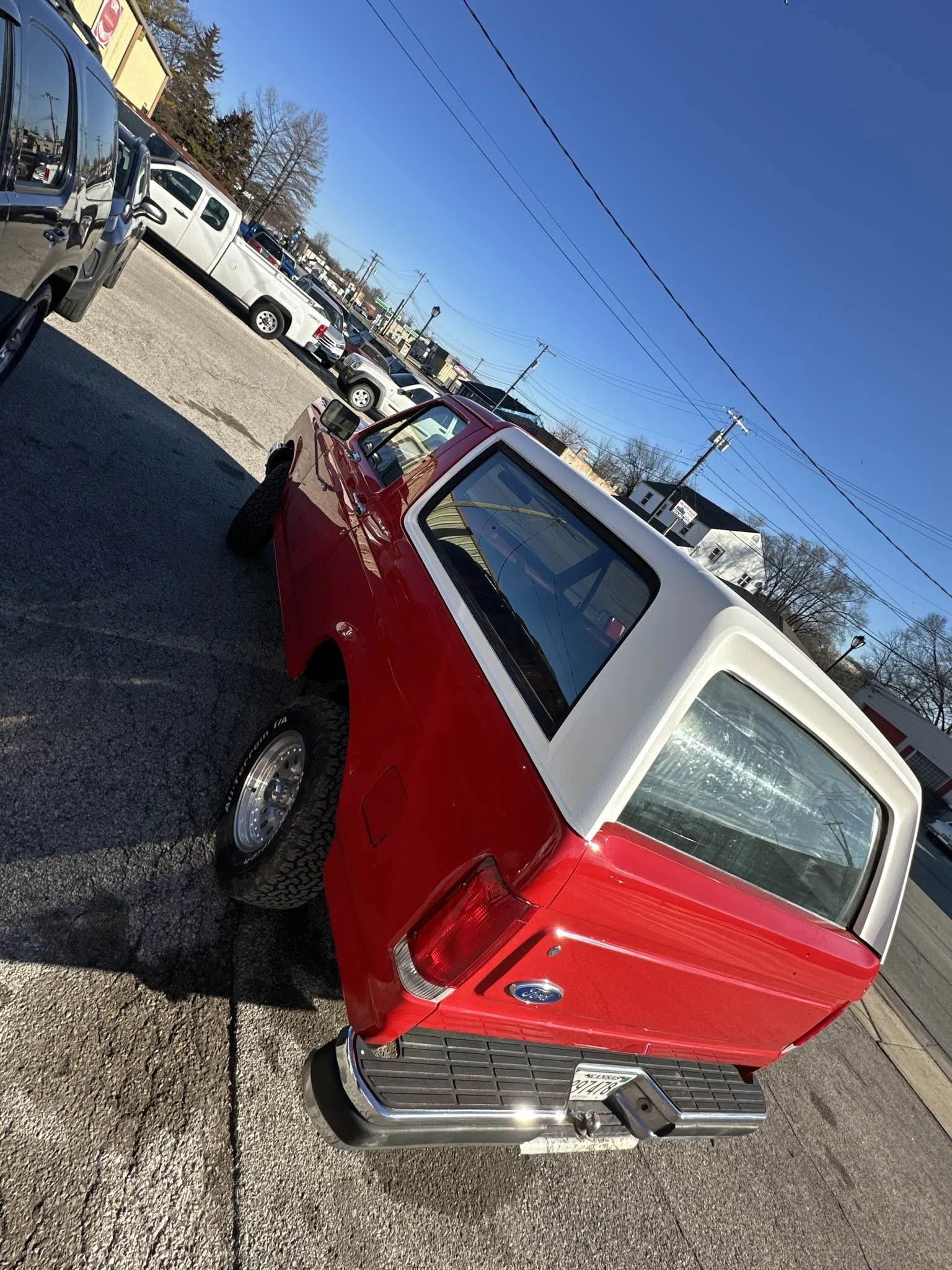 Red and white vintage Ford truck parked in a lot with other vehicles, under a clear blue sky.