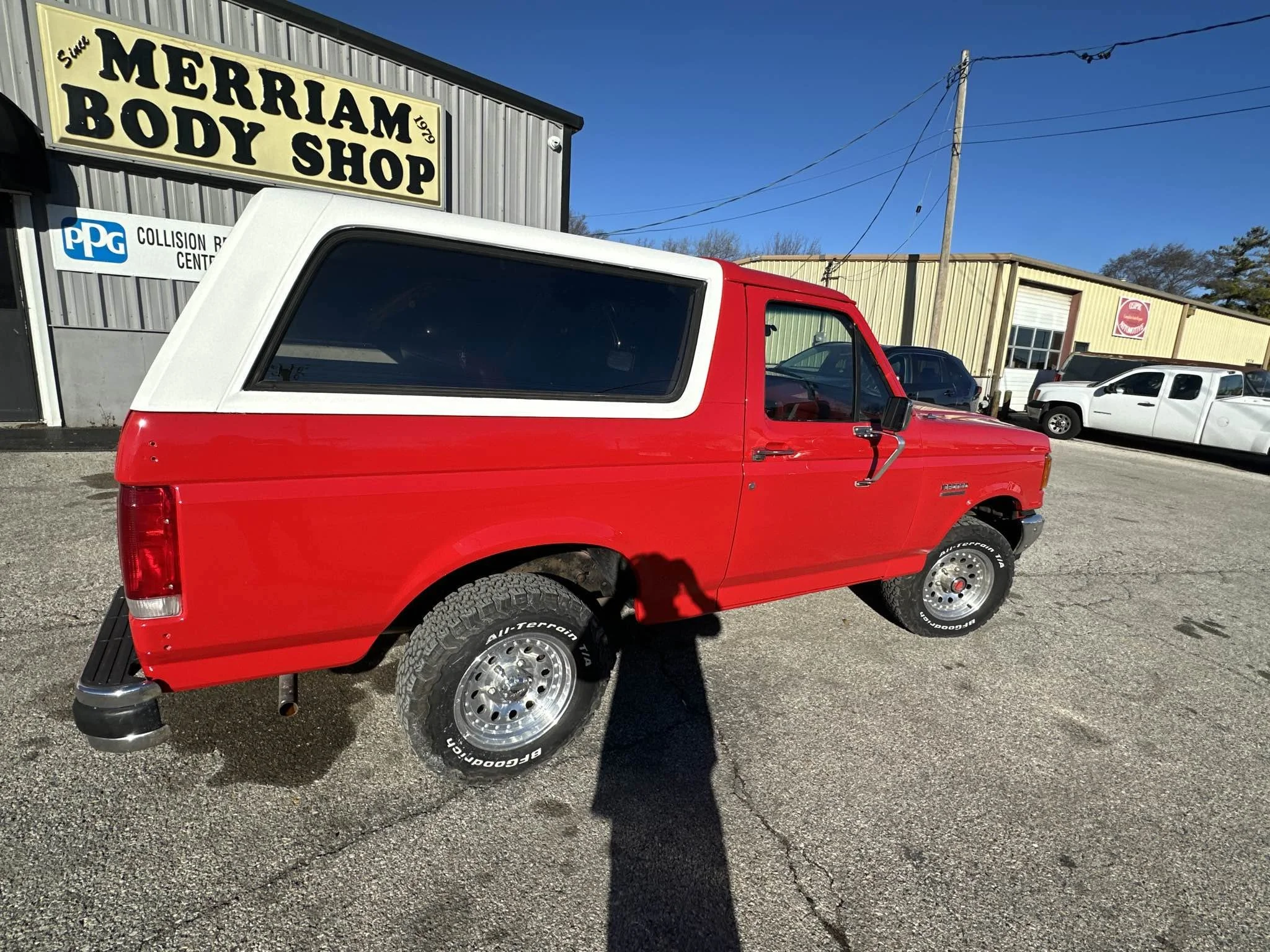 Red pickup truck with a white camper shell parked outside a body shop and collision center.