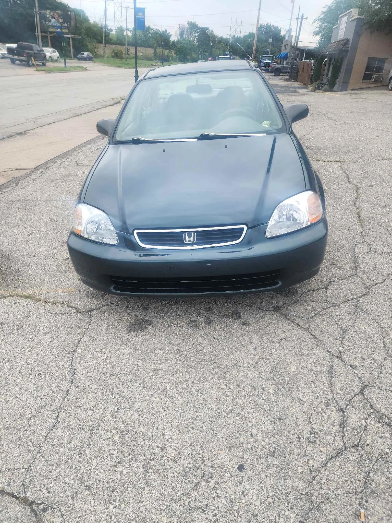 Front view of a dark blue Honda Civic parked on a cracked asphalt surface in an urban area.