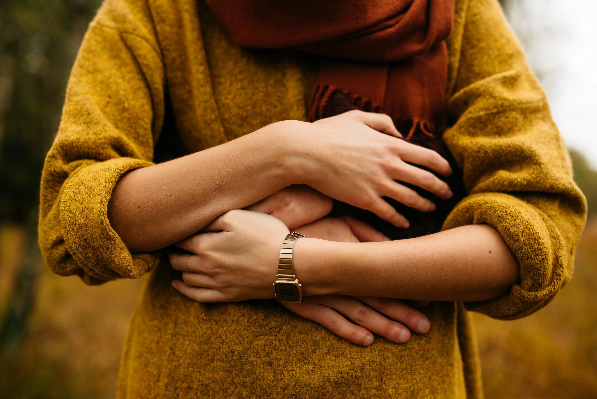 Person with yellow sweater and red scarf being hugged from behind. Hand's are overlapping.