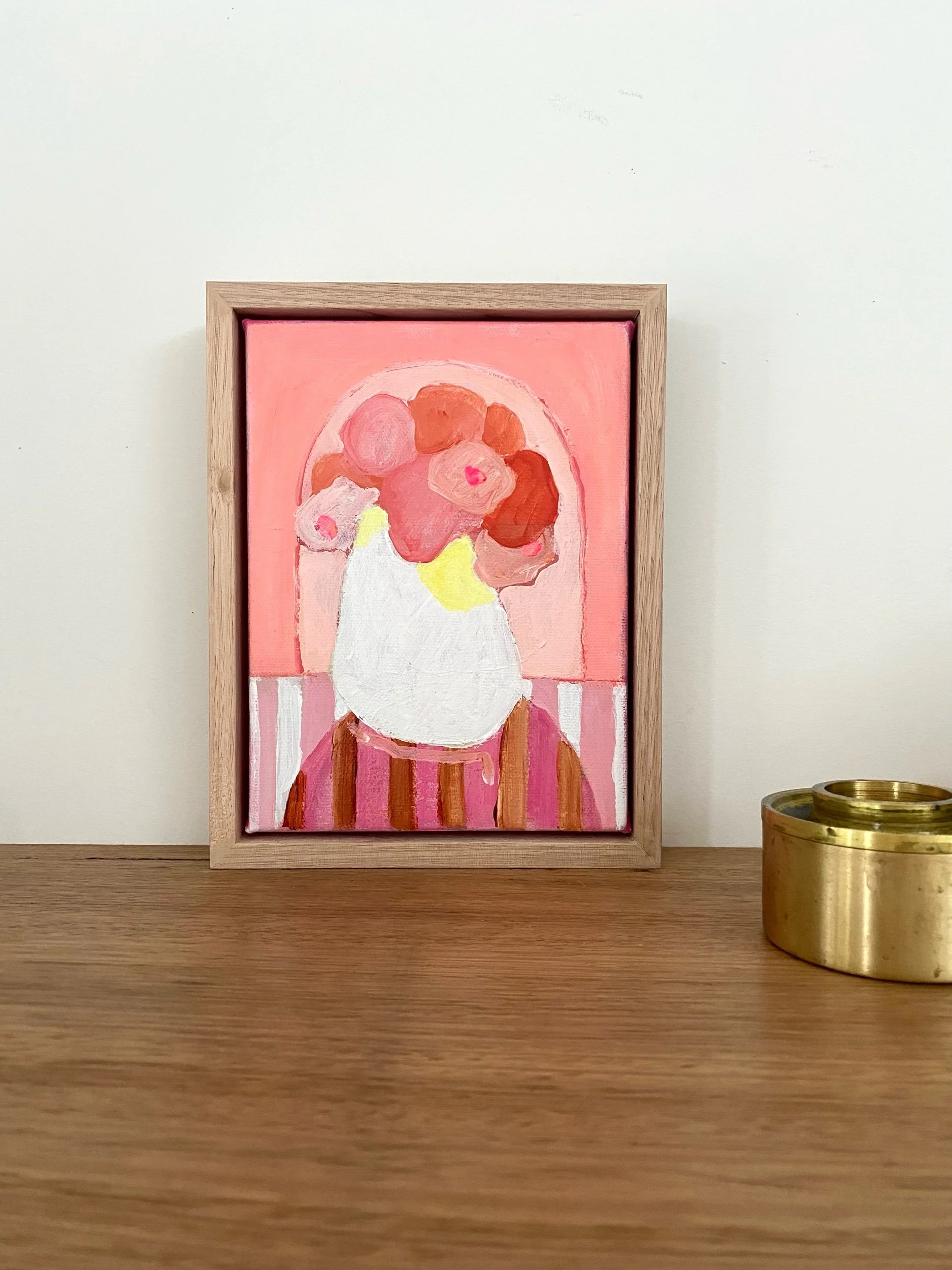 A framed abstract painting of flowers in warm colors on a wooden table next to a brass candle holder.