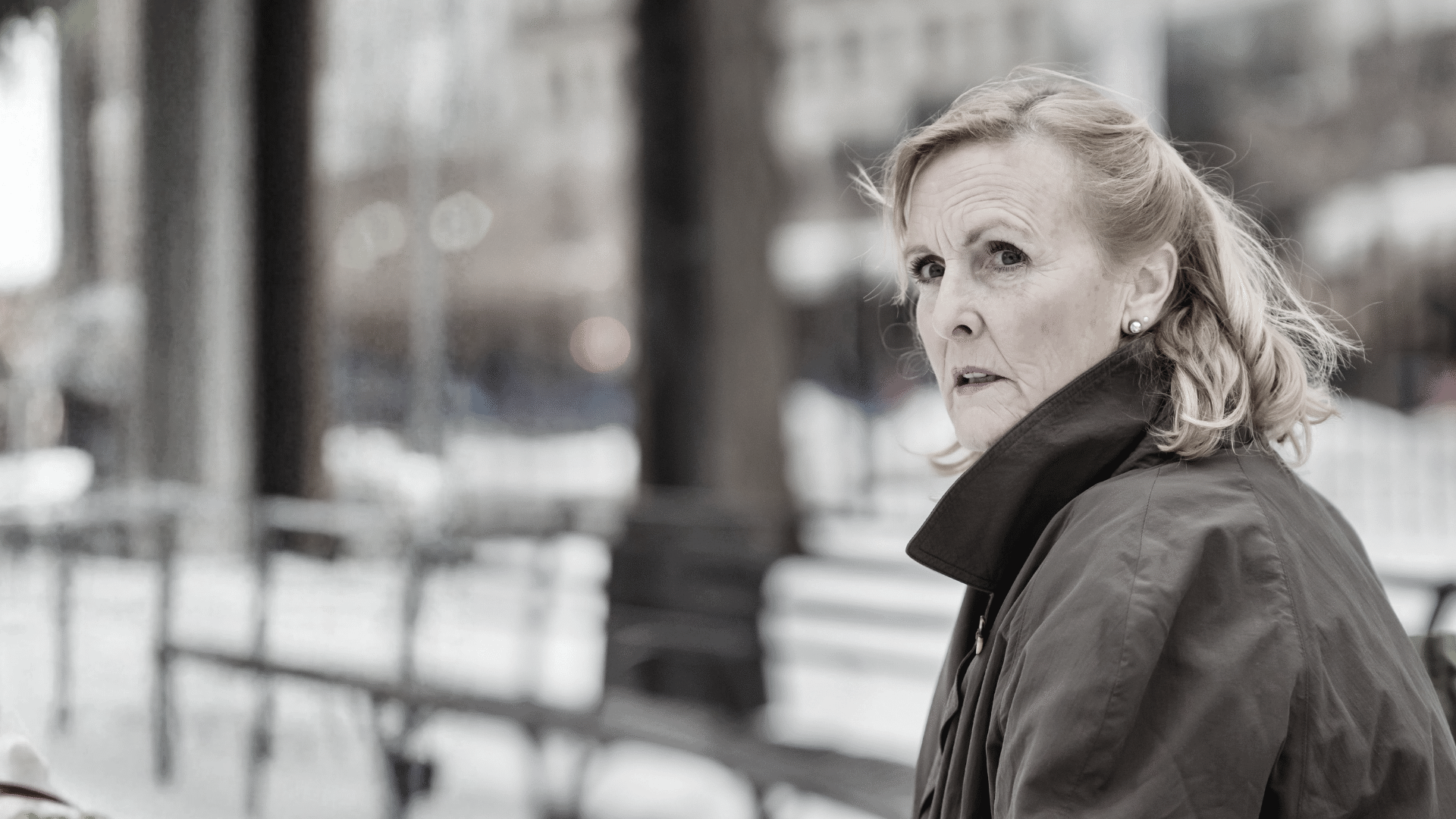 Ältere Frau in brauner Jacke sieht angstvoll zur Seite