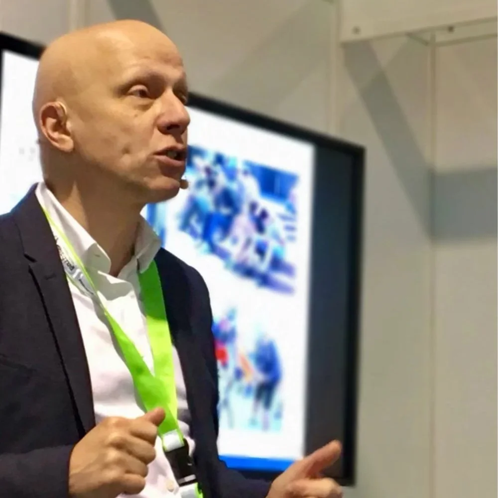Man in business outfit standing and talking in front of a screen